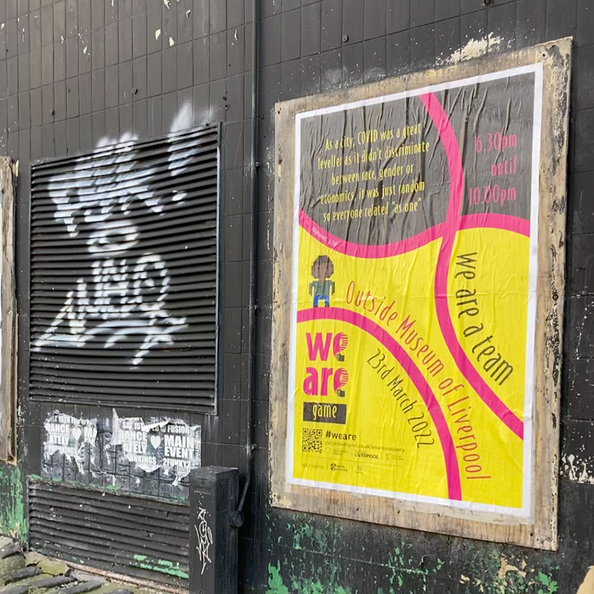 An image of a poster pasted on to a wall with other posters. The poster is yellow and grey with pink DNA strands on it. It's advertising the game