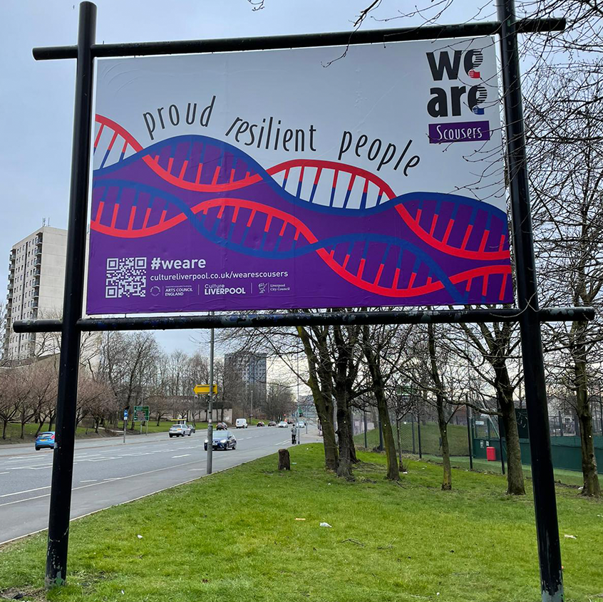 An image of a billboard showing the stylised DNA strands in Red, Blue and white horozontally on a purple back ground with the words proud, resilient, people above. The words we are are large and grey on the right and underneath in a purple box it say