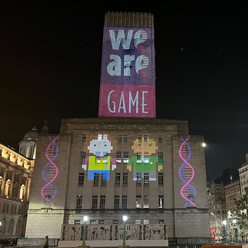 An image of the Birkenhead Tunnel vent on the Strand in Liverpool with We are game projected on to it. There are strands of DNA on either side of two pixel characters from the game