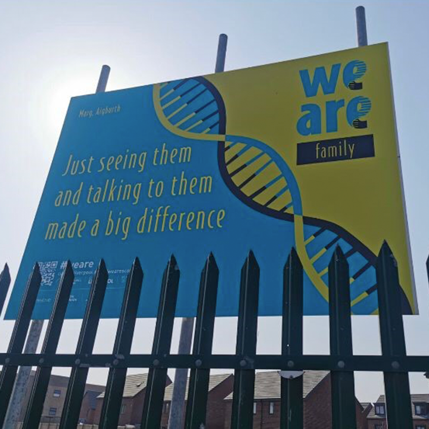 An image of a billboard showing the stylised DNA strands in grey, yellow and light blue. The words we are are large and blue on the right and underneath in a grey box it says family