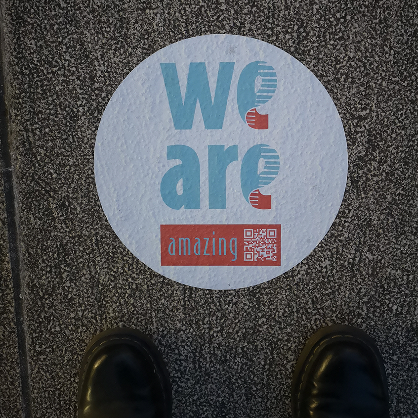 An image of the toes of some boots standing in front of a circular floor vinyl saying we are amazing. 