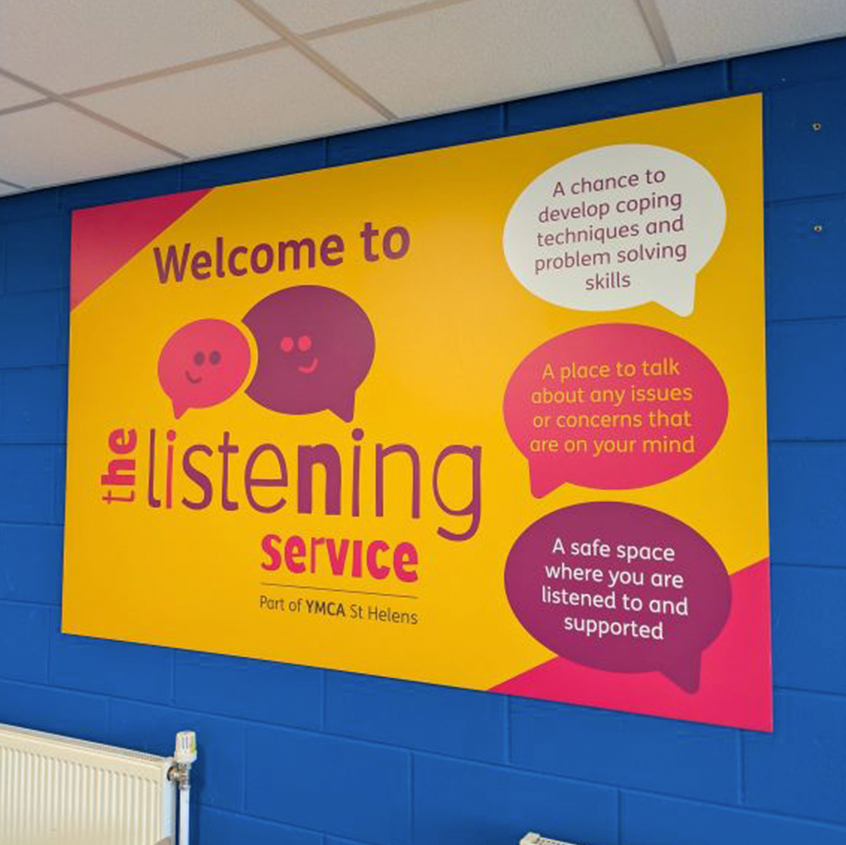 An image of a wall vinyl in St Helens YMCA. The background is yellow with welcome to above the listening service logo large on the left. On the right are 3 speech bubbles with service information in