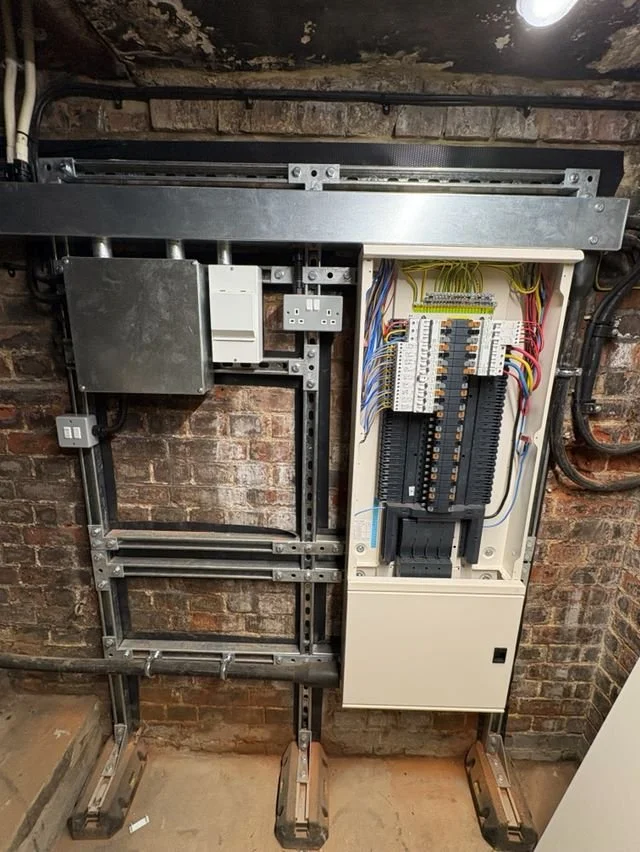 Electrical control panel with wiring, circuit breakers, and a metal enclosure, mounted on a brick wall.