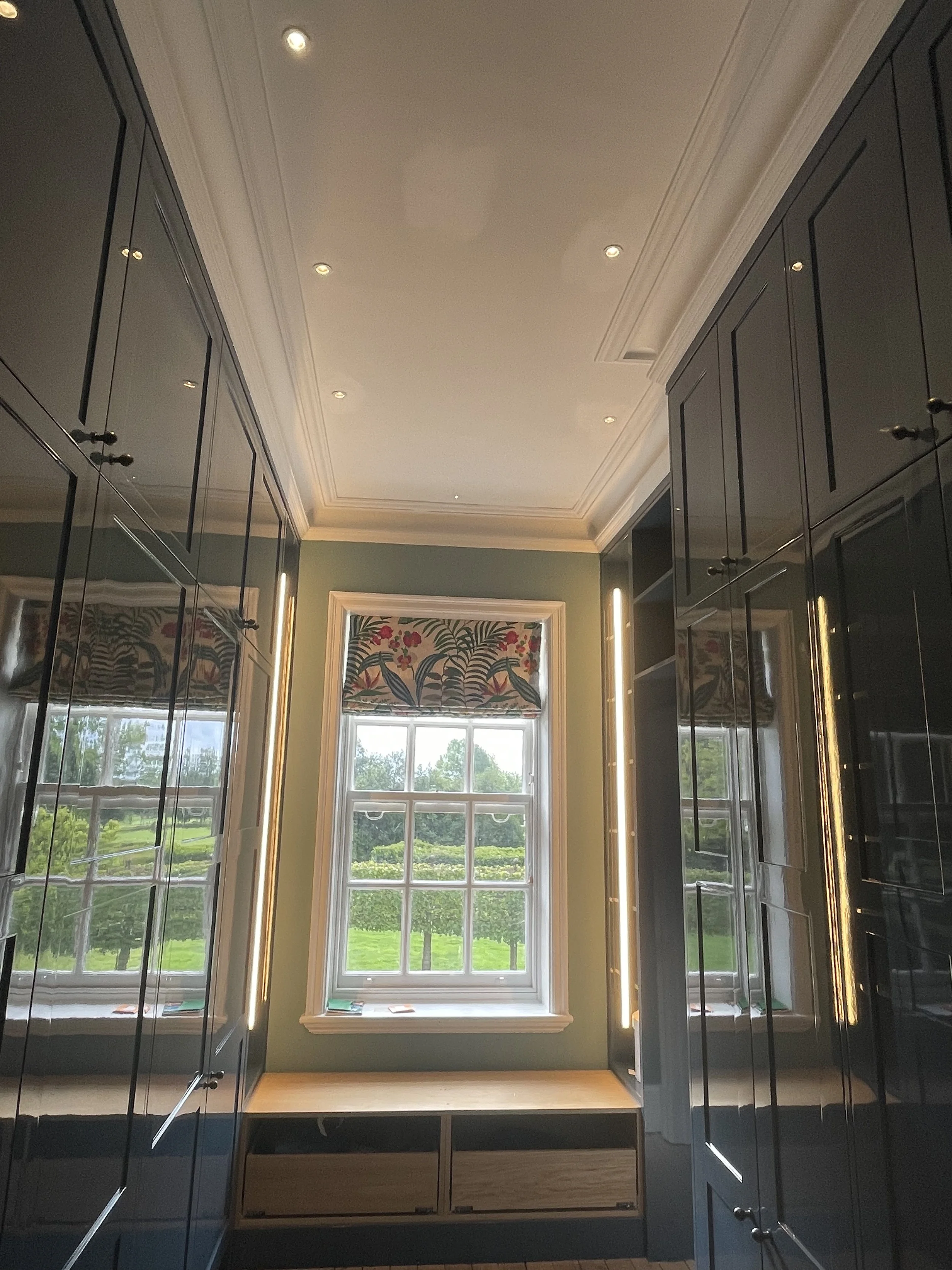 View of a window with colorful floral and bird wallpaper outside, surrounded by navy blue cabinetry in a room with beige ceiling and crown molding.