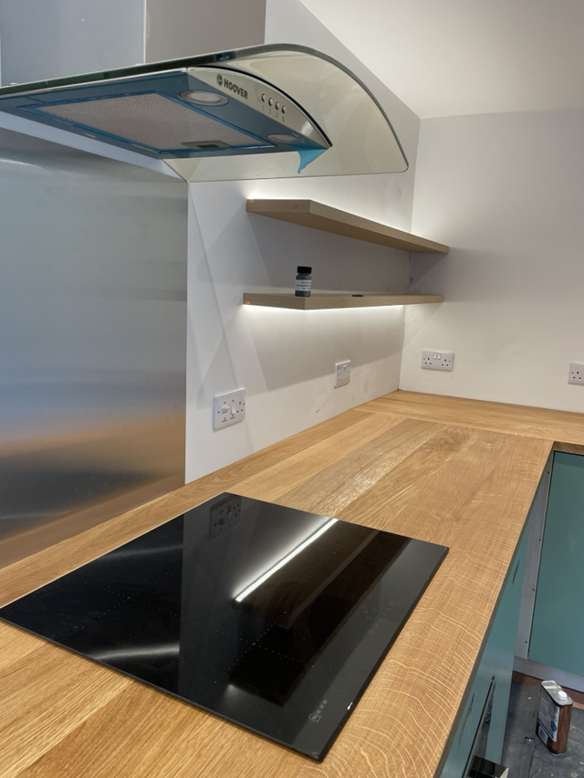 Modern kitchen with a black electric stove, wooden countertop, and white wall with two floating wooden shelves.