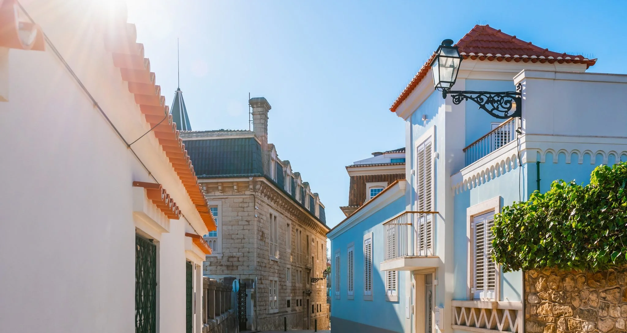 Bright blue sky above colorful Mediterranean-style buildings with terracotta roofs and decorative wrought iron details.