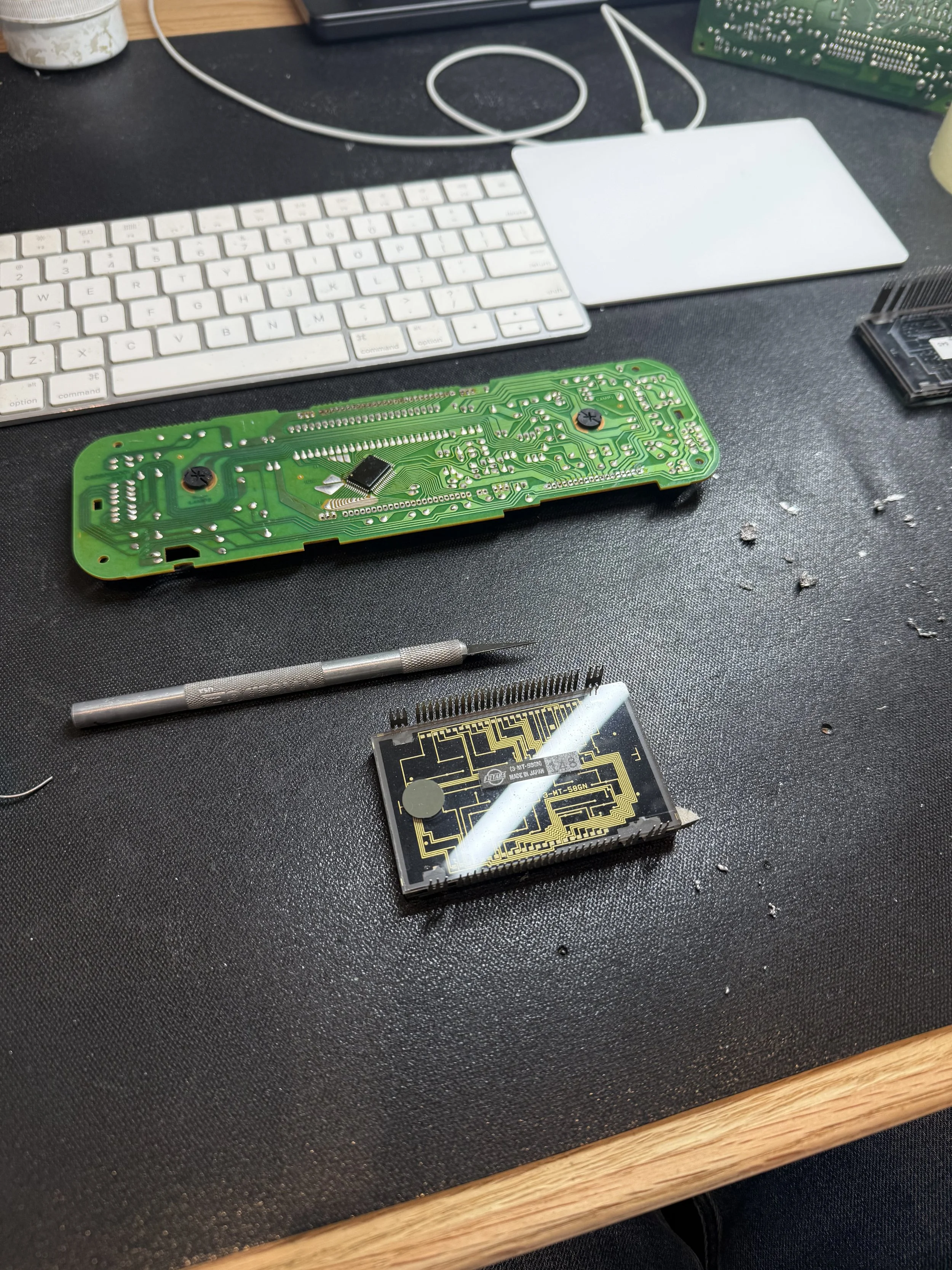 Disassembled electronic circuit board, keyboard, and tools on a black work surface.