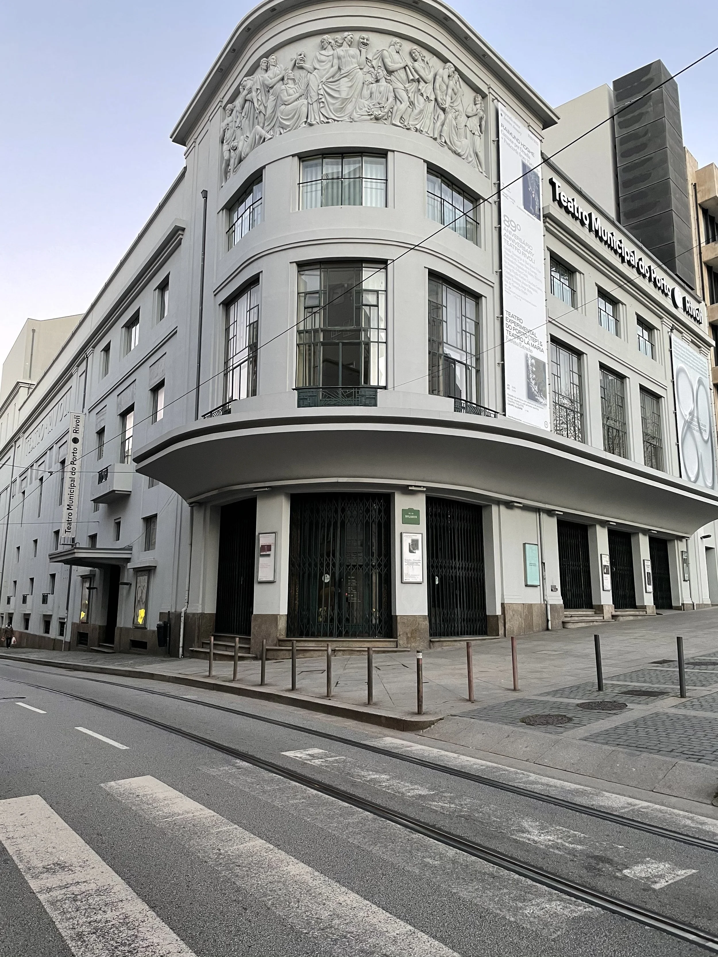 A film and photo location in Portugal from walnut films, A white building with curved windows and a bas-relief sculpture at the top, with banners on the side indicating it is the Teatro Municipal do Porto in Portugal. 