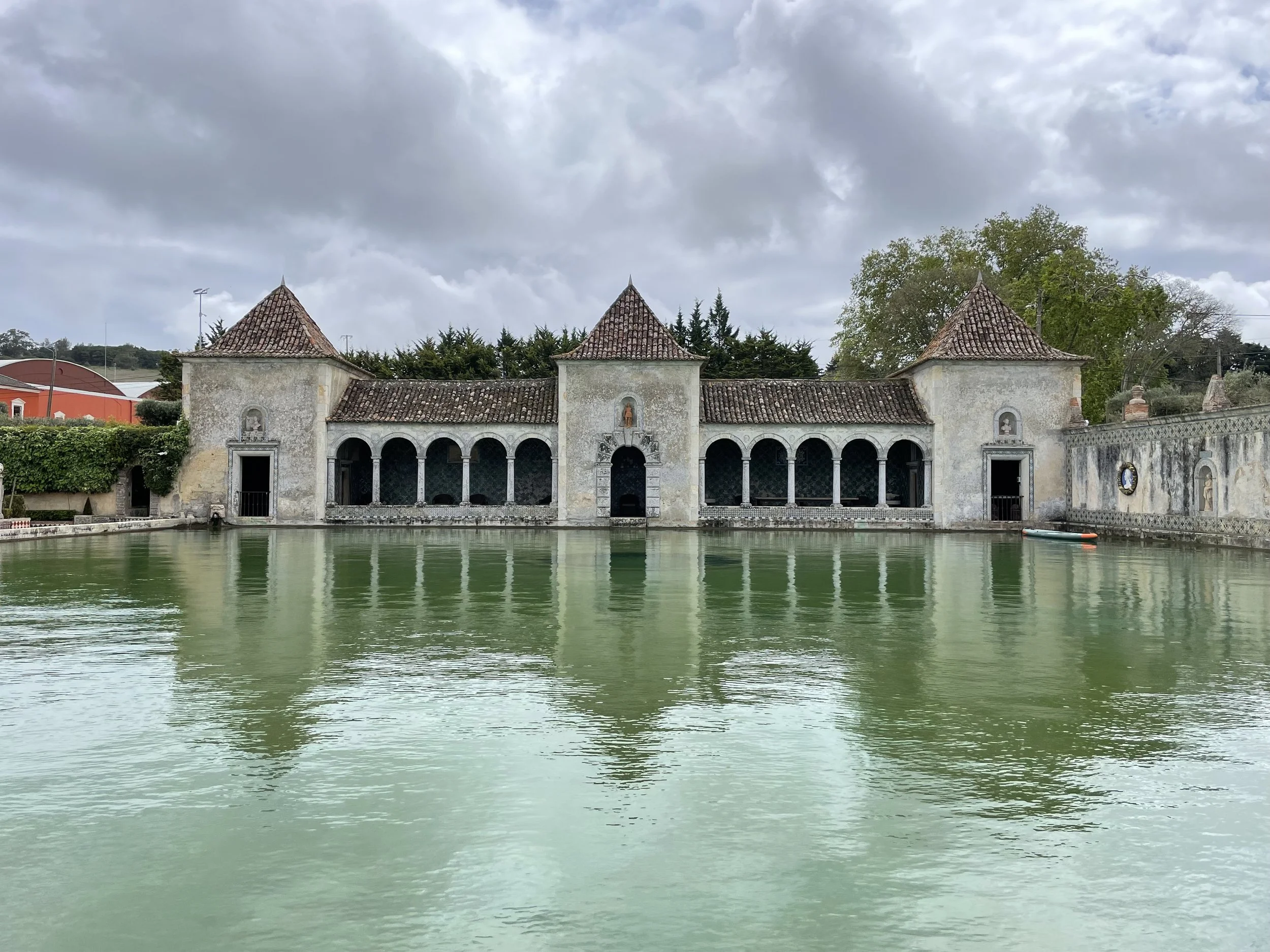 A film and photo location in Portugal from walnut films, A historic building with a water feature in front, featuring arched windows and a tiled roof, under cloudy skies.