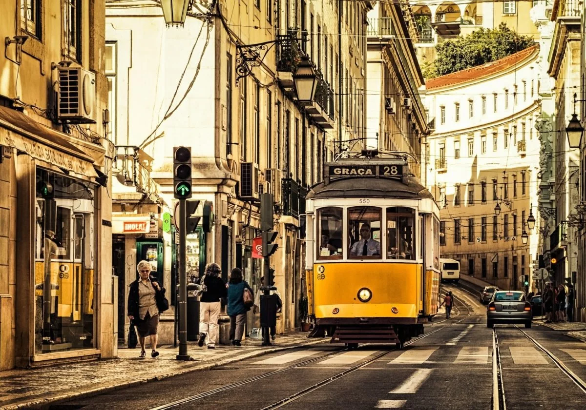 A film and photo location in Portugal from walnut films, A yellow tram on a city street with pedestrians walking and buildings lining the street.