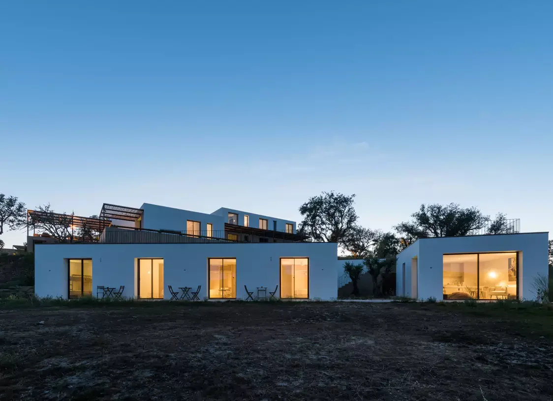 A film and photo location in Portugal from walnut films, Modern white house with large glass windows in the evening, trees in the background, outdoor seating on the patio