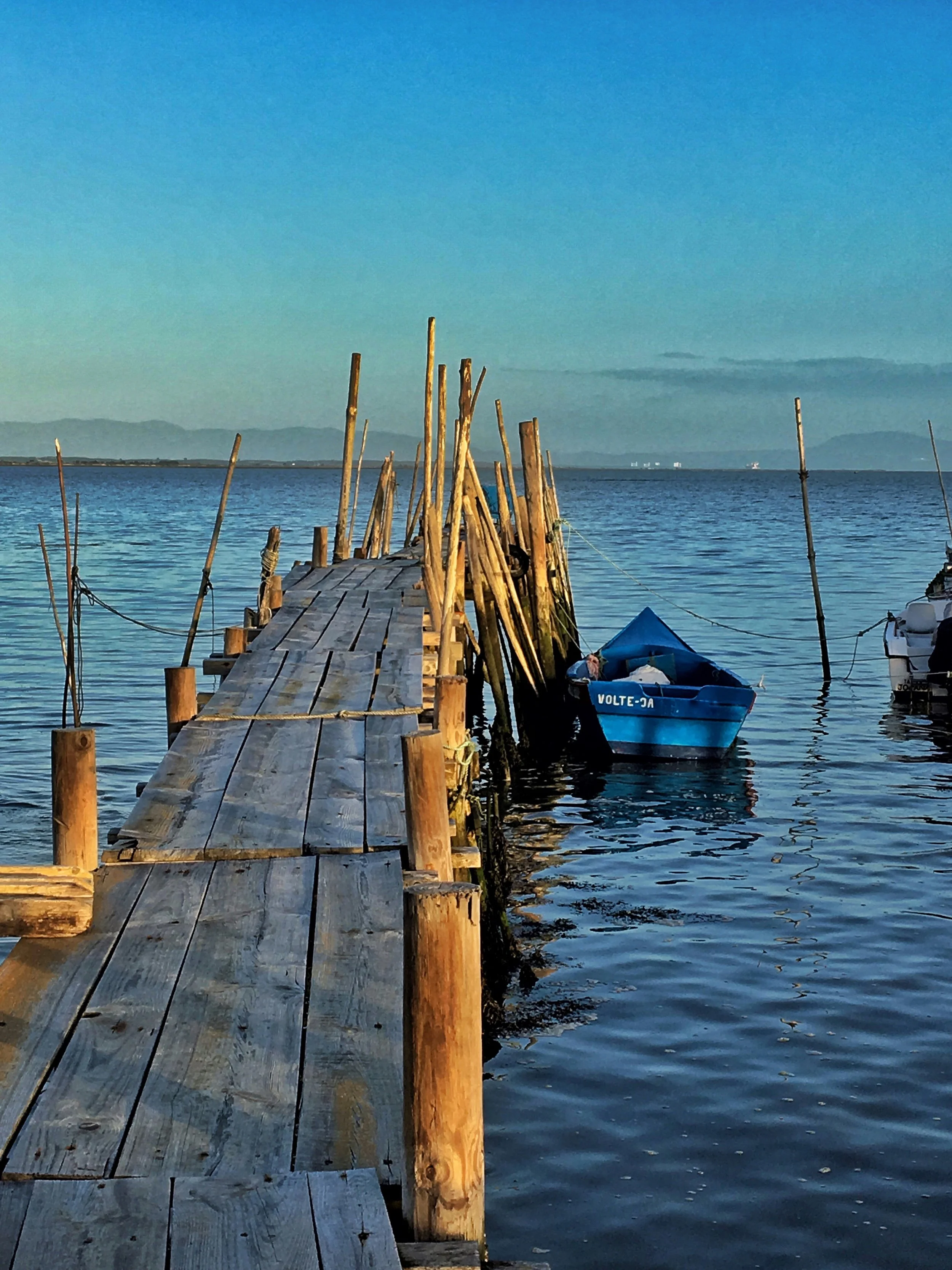 A film and photo location in Portugal from walnut films, A wooden dock extending into a calm body of water with mountains and a blue sky in the background.