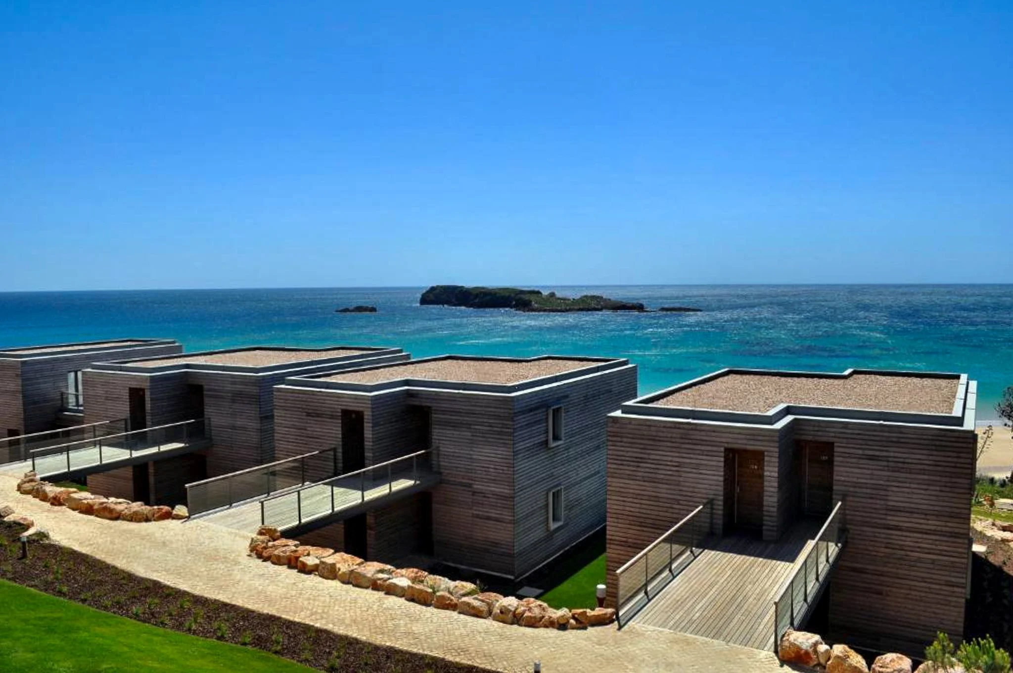 A film and photo location in Portugal from walnut films, Modern houses with flat roofs overlooking the ocean and a small rocky island in the background.