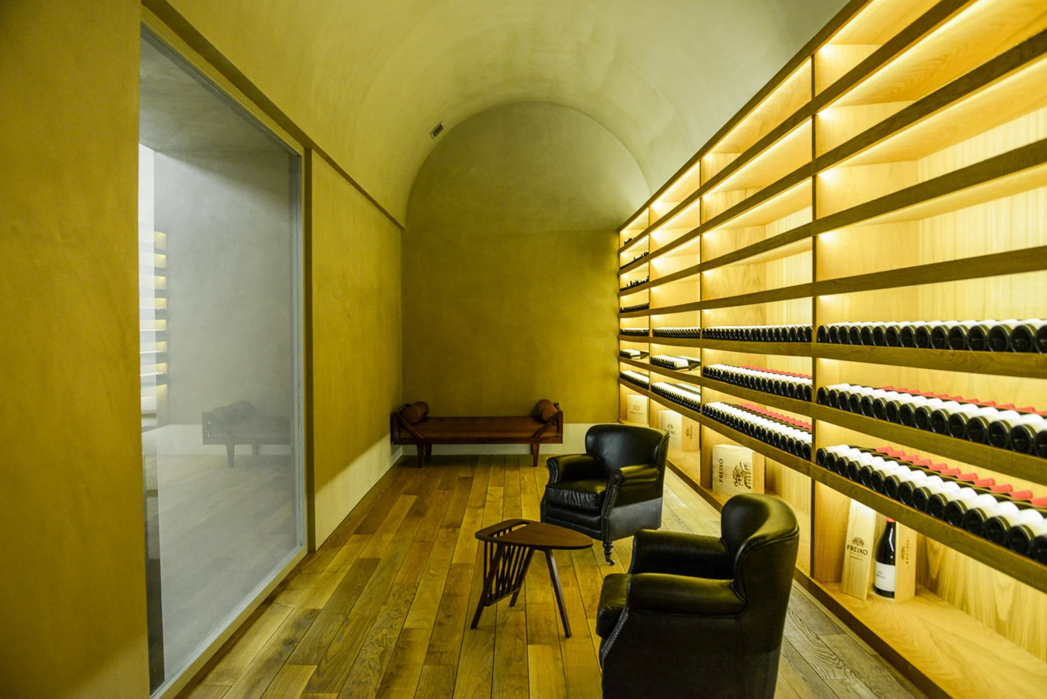 A film and photo location in Portugal from walnut films, Wine bottles stored on wooden shelves in a cozy wine cellar or tasting room with chairs and a bench.