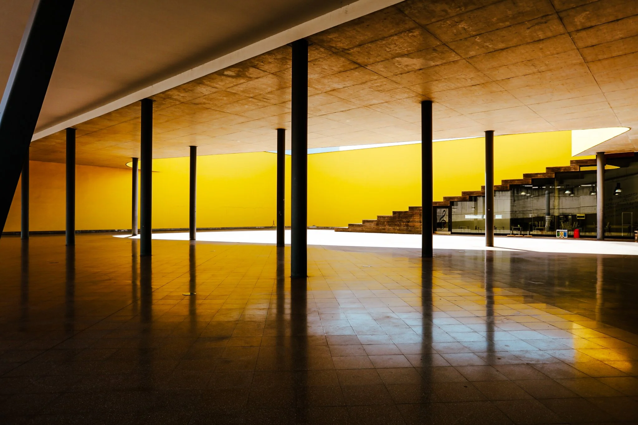 A film and photo location in Portugal from walnut films, Un interieur avec un plafond en bois, plusieurs colonnes noires, un escalier en bois, et un mur jaune vif à l'arrière.