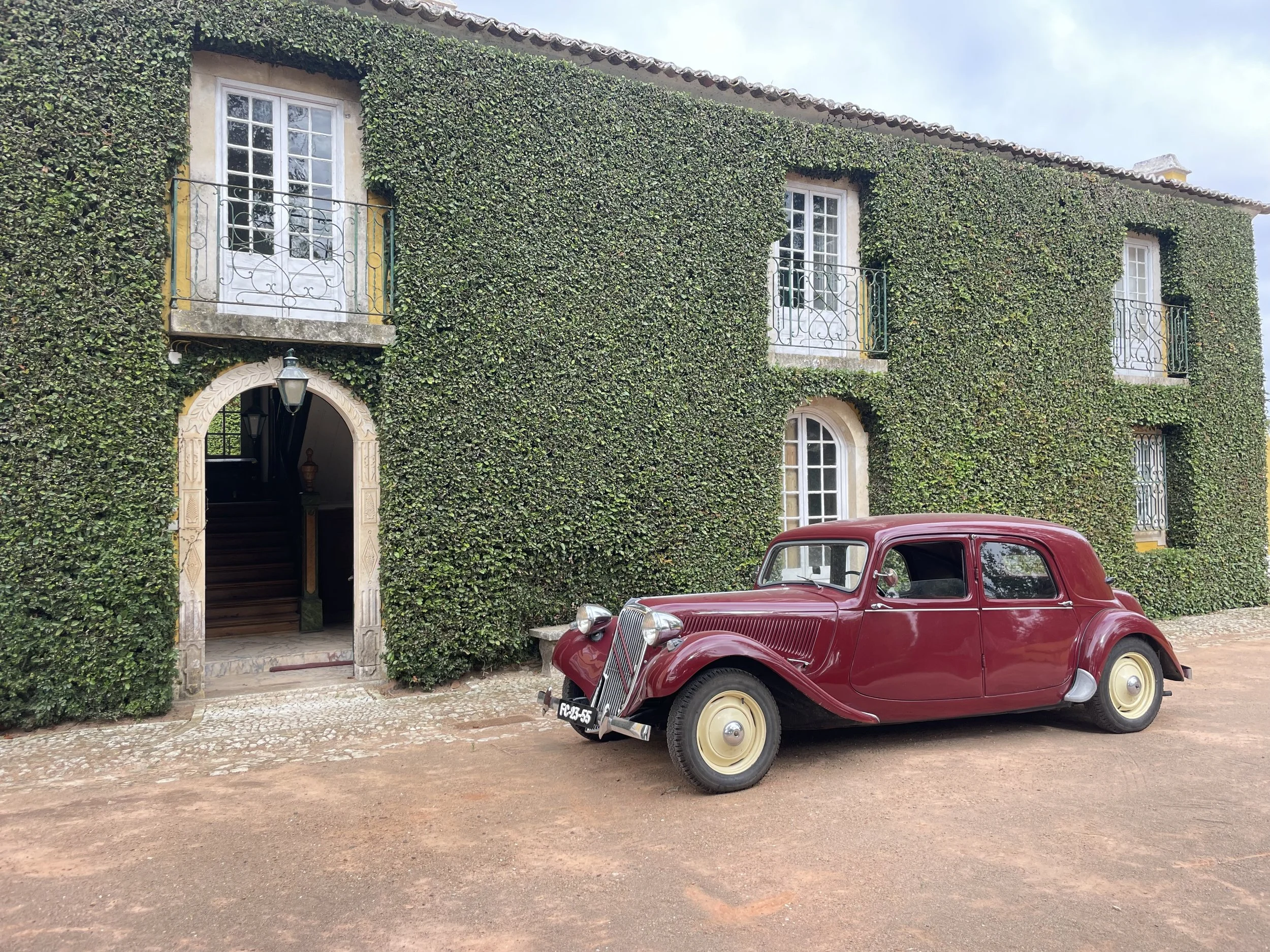 A film and photo location in Portugal from walnut films, A vintage red car parked in front of a building covered in green ivy with multiple windows and small balconies.