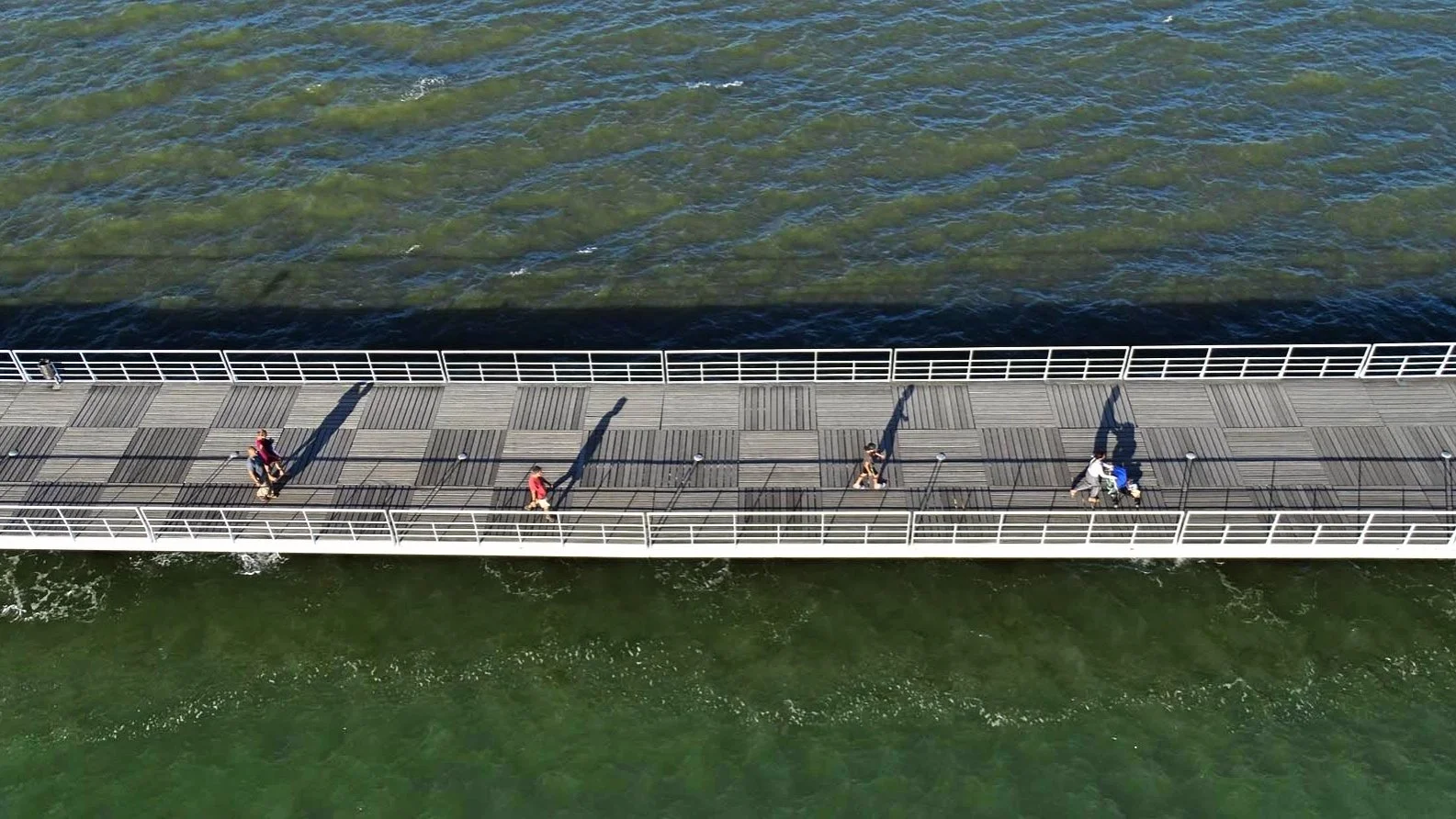 A film and photo location in Portugal from walnut films, Aerial view of a pier with people walking and biking, over green and blue water.