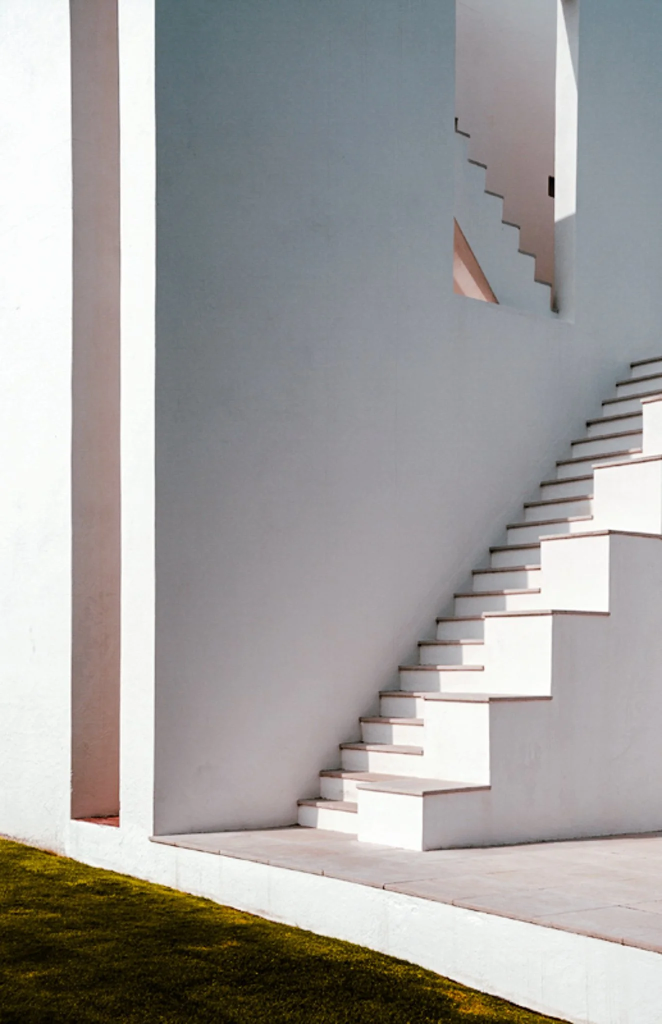 A film and photo location in Portugal from walnut films, Modern white building with a staircase carved into the wall and a triangular window, with a patch of grass in the foreground.