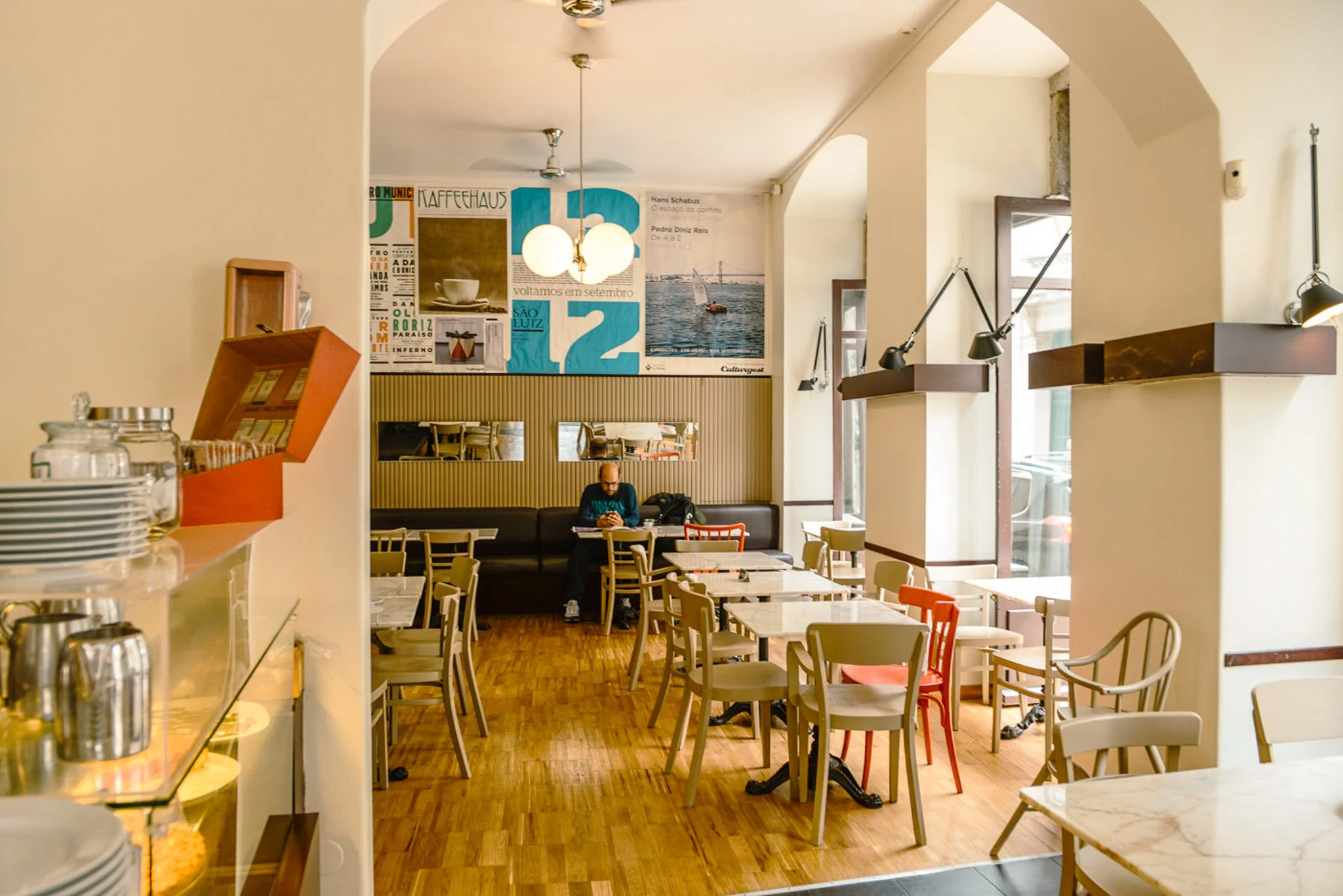 A film and photo location in Portugal from walnut films, Interior of a cozy cafe with tables and chairs, wall decorations including posters, and a large window letting in natural light.