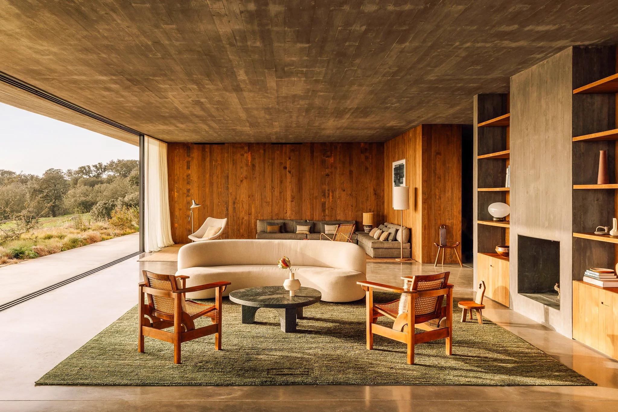 A film and photo location in Portugal from walnut films, Modern living room with large open sliding glass doors, wooden wall and ceiling, and mid-century furniture including a sofa, armchairs, and a coffee table, with a view of a natural