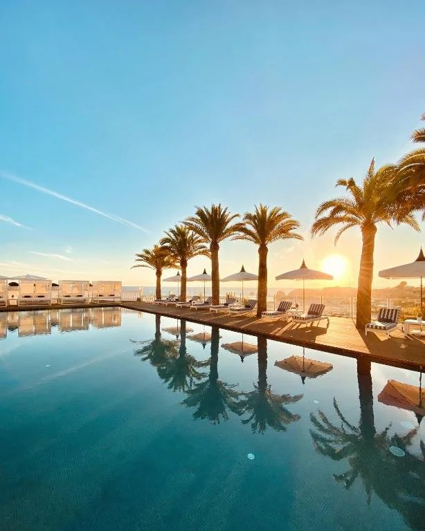 A film and photo location in Portugal from walnut films, A poolside scene with palm trees, lounge chairs, umbrellas, and a sunset sky.