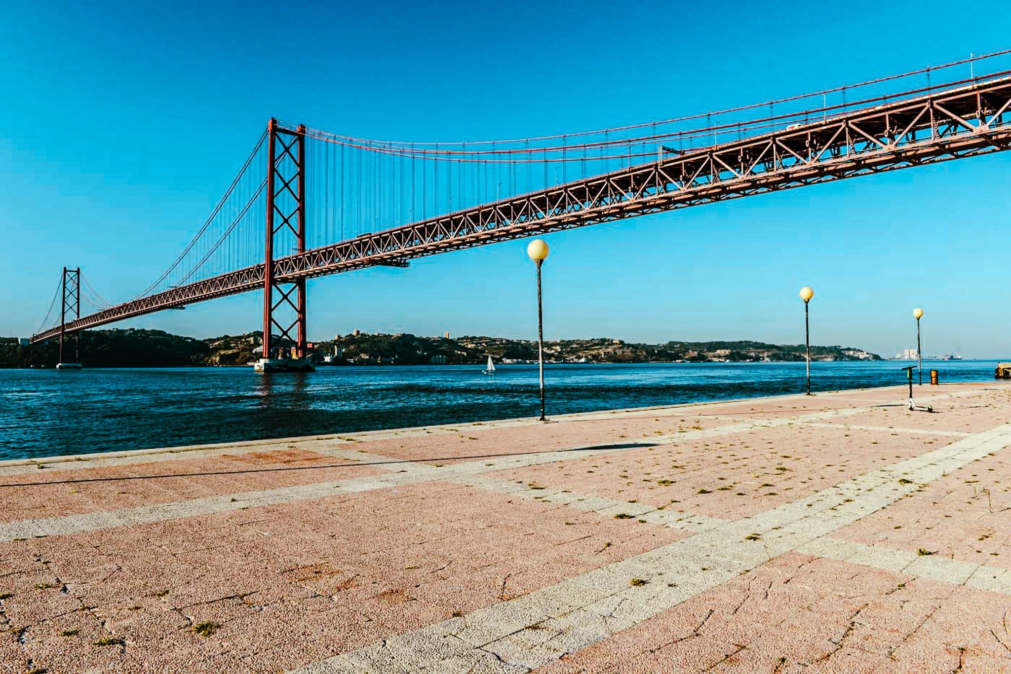 A film and photo location in Portugal from walnut films, A bridge spans over a body of water, with a clear blue sky above and lamp posts along a waterfront promenade.