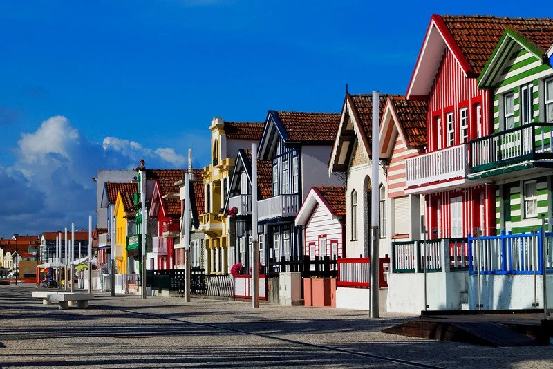 A film and photo location in Portugal from walnut films, Colorful houses with striped and solid exterior walls in a seaside town under a blue sky with clouds.