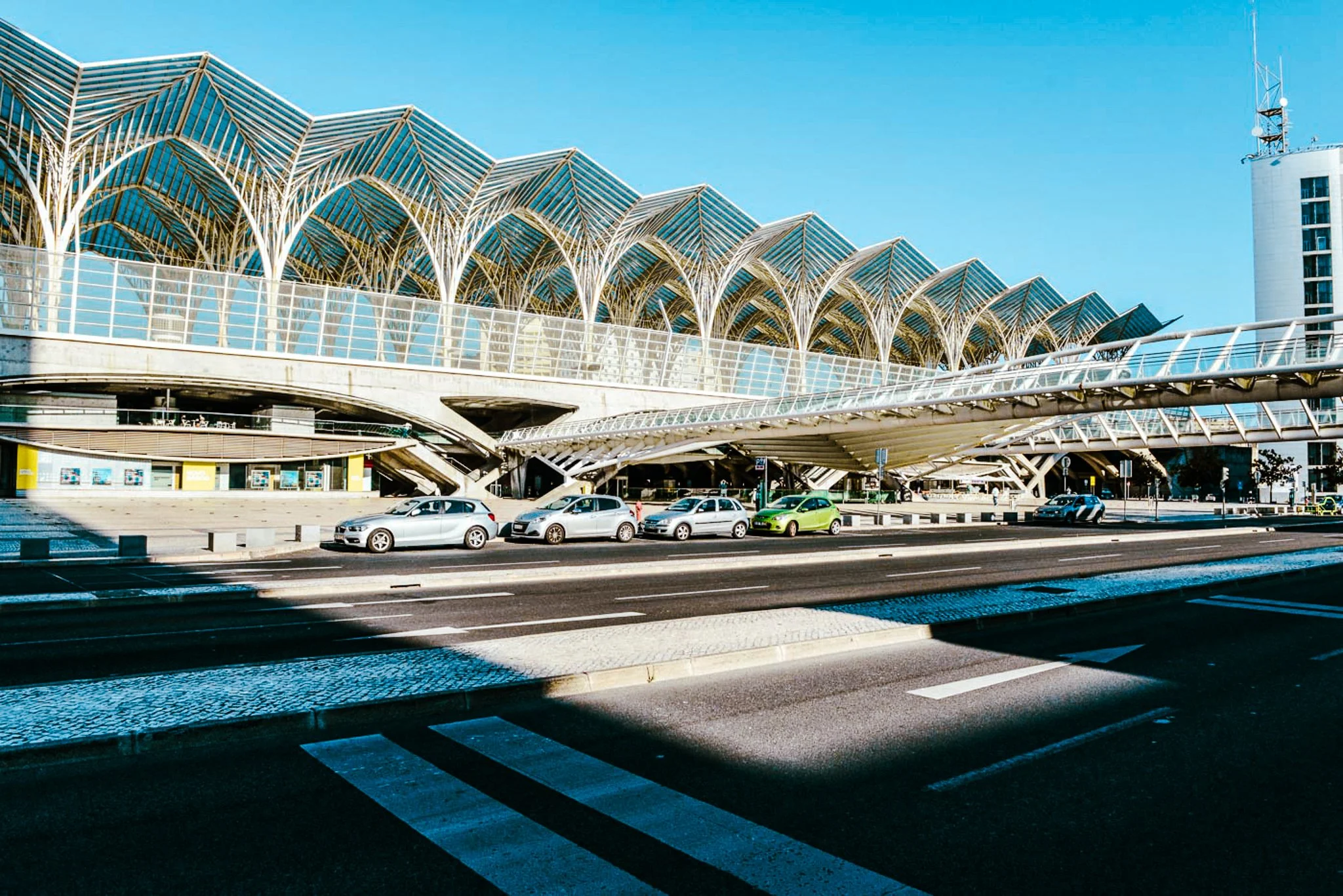 A film and photo location in Portugal from walnut films, Modern building with architectural roof design and a parking lot with cars in the foreground, under a clear blue sky.