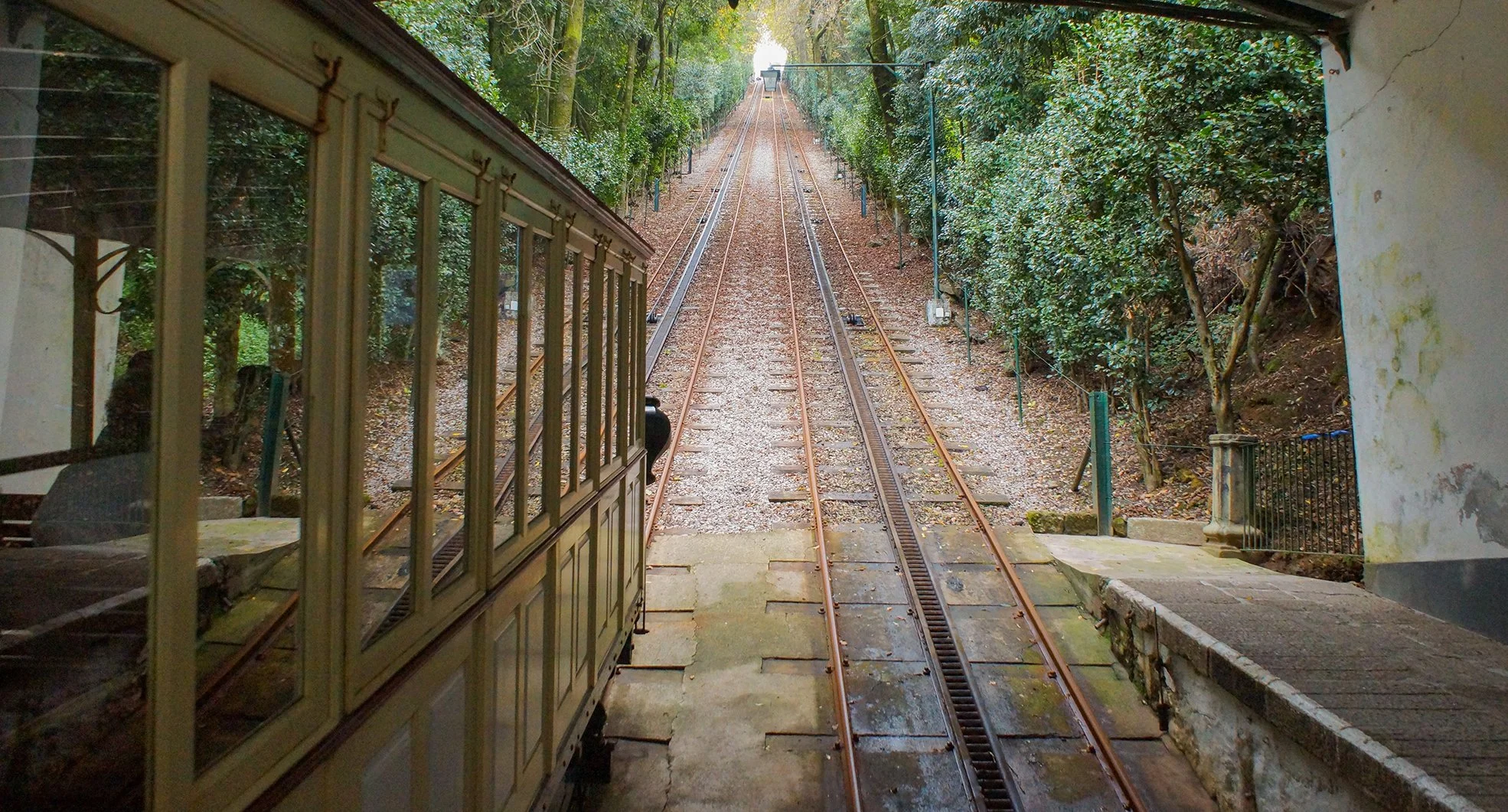 A film and photo location in Portugal from walnut films, View from a train station platform showing a train track leading into a wooded hillside with trees and foliage on both sides.