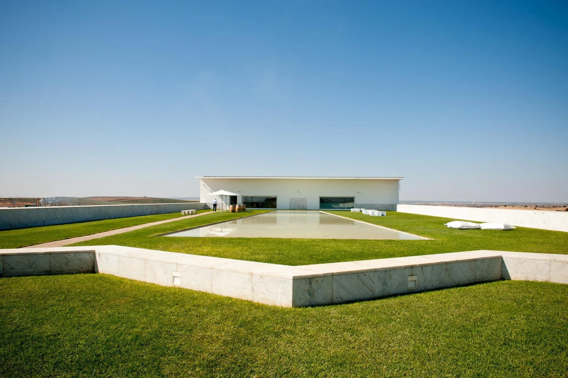 A film and photo location in Portugal from walnut films, Modern white building with a flat roof, surrounded by a green lawn with a reflective pool in the foreground, set against a clear blue sky.