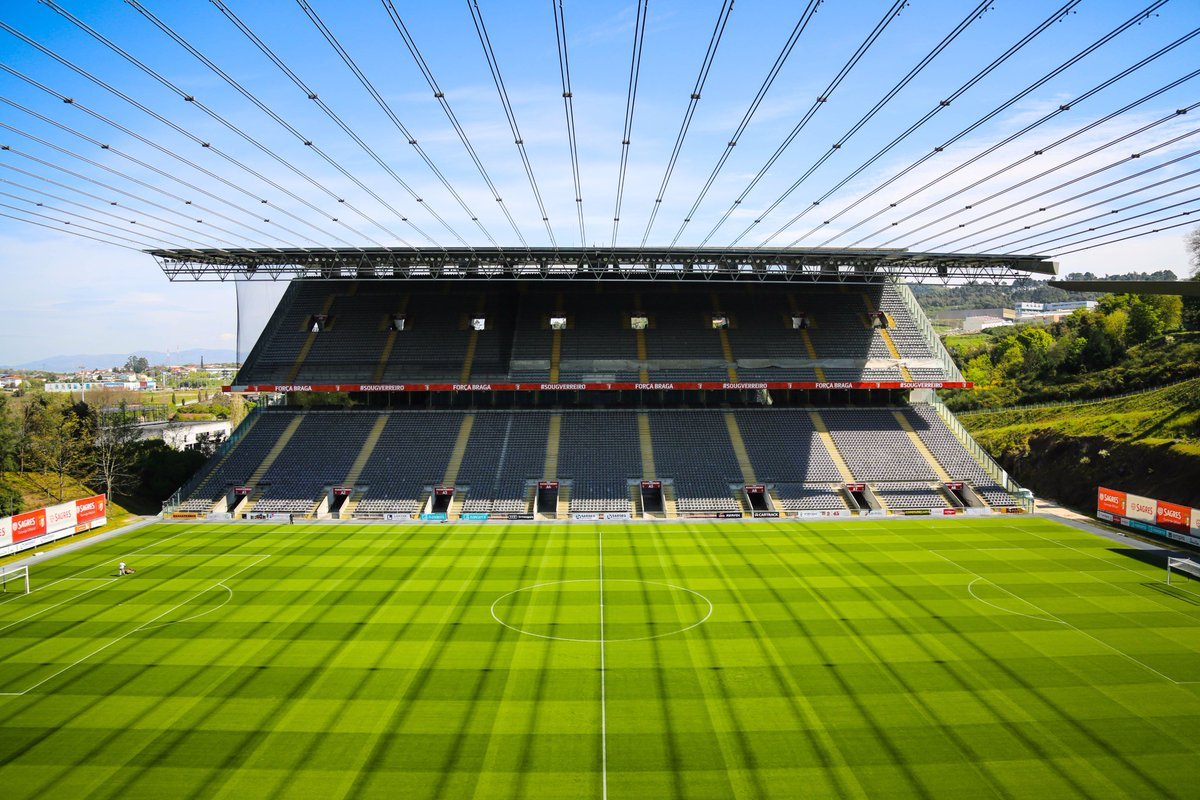 A film and photo location in Portugal from walnut films, Empty football stadium with a green field, seats, and a roof with cables overhead.