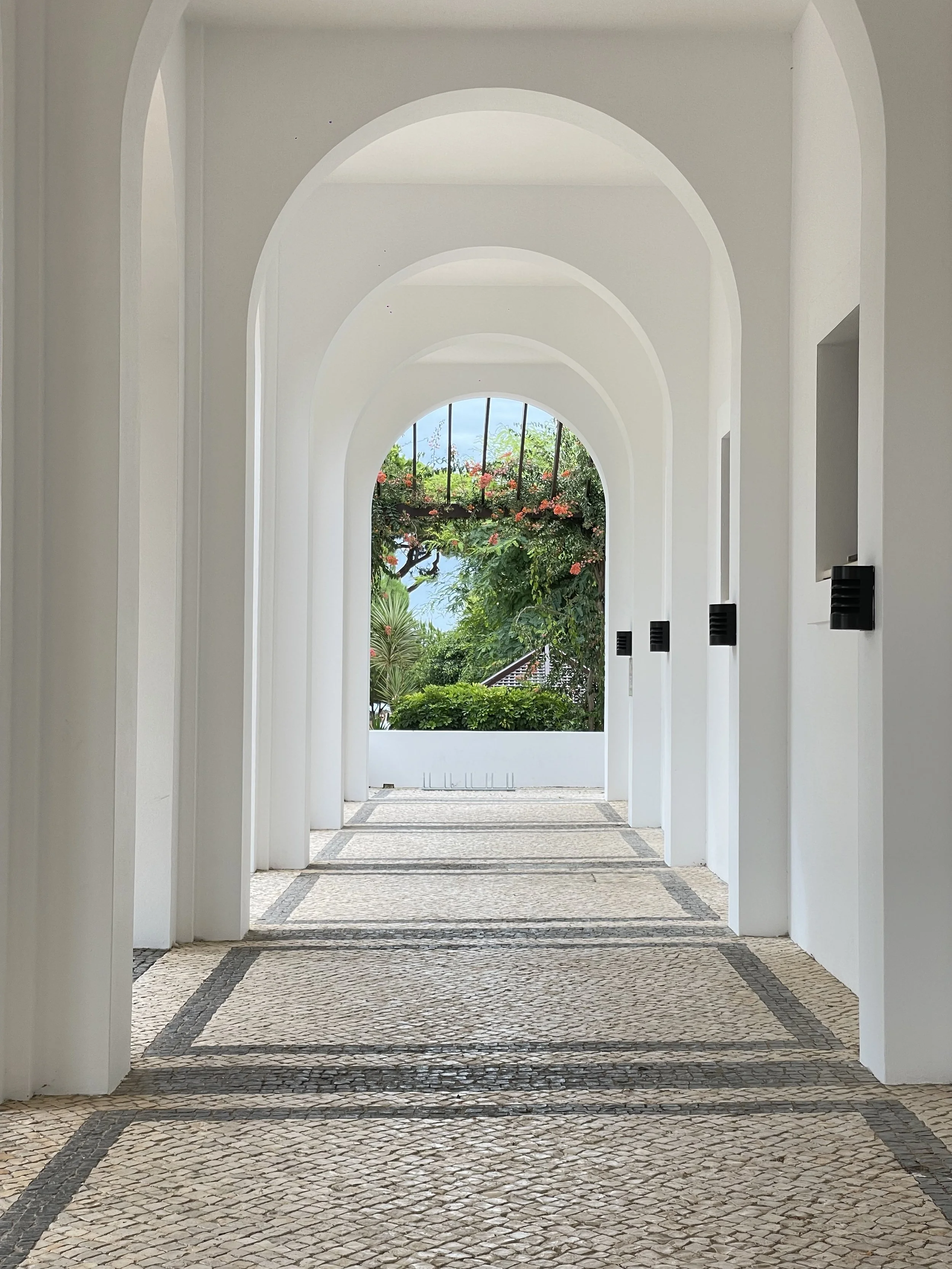 A film and photo location in Portugal from walnut films, A white arched walkway with multiple archways leading to a garden view with trees and flowers.