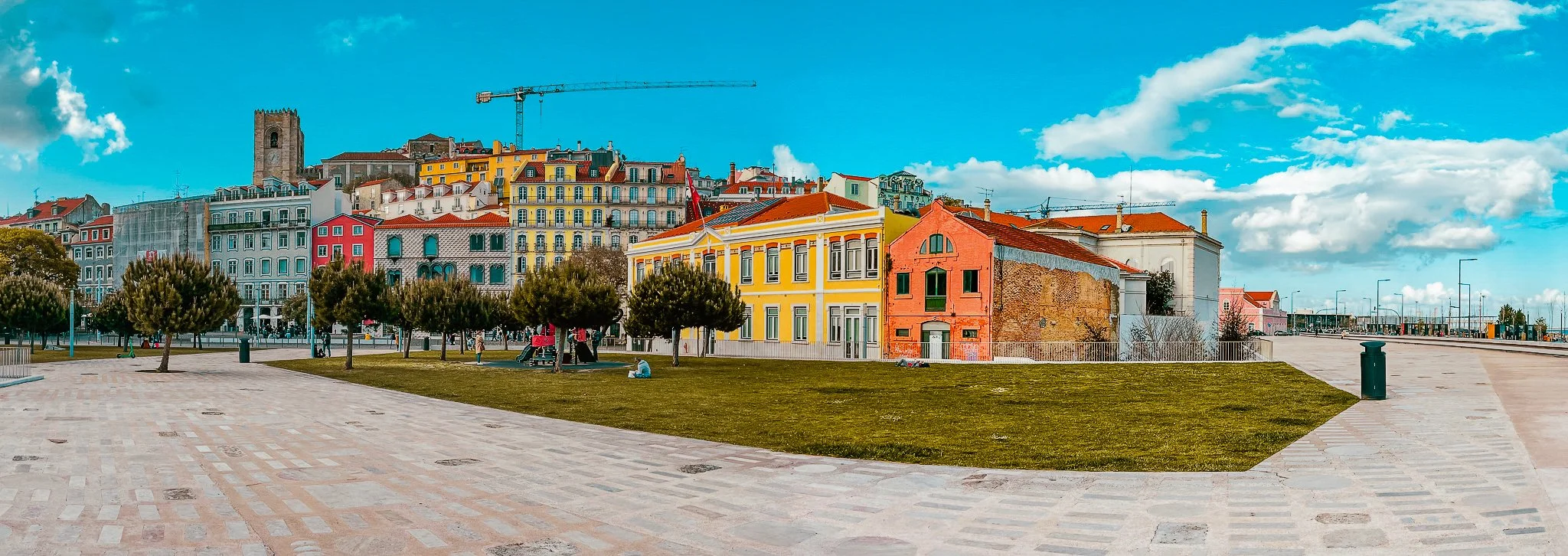 A film and photo location in Portugal from walnut films, Colorful buildings along a hillside under a partly cloudy sky, with a park in the foreground and construction crane visible in the distance.