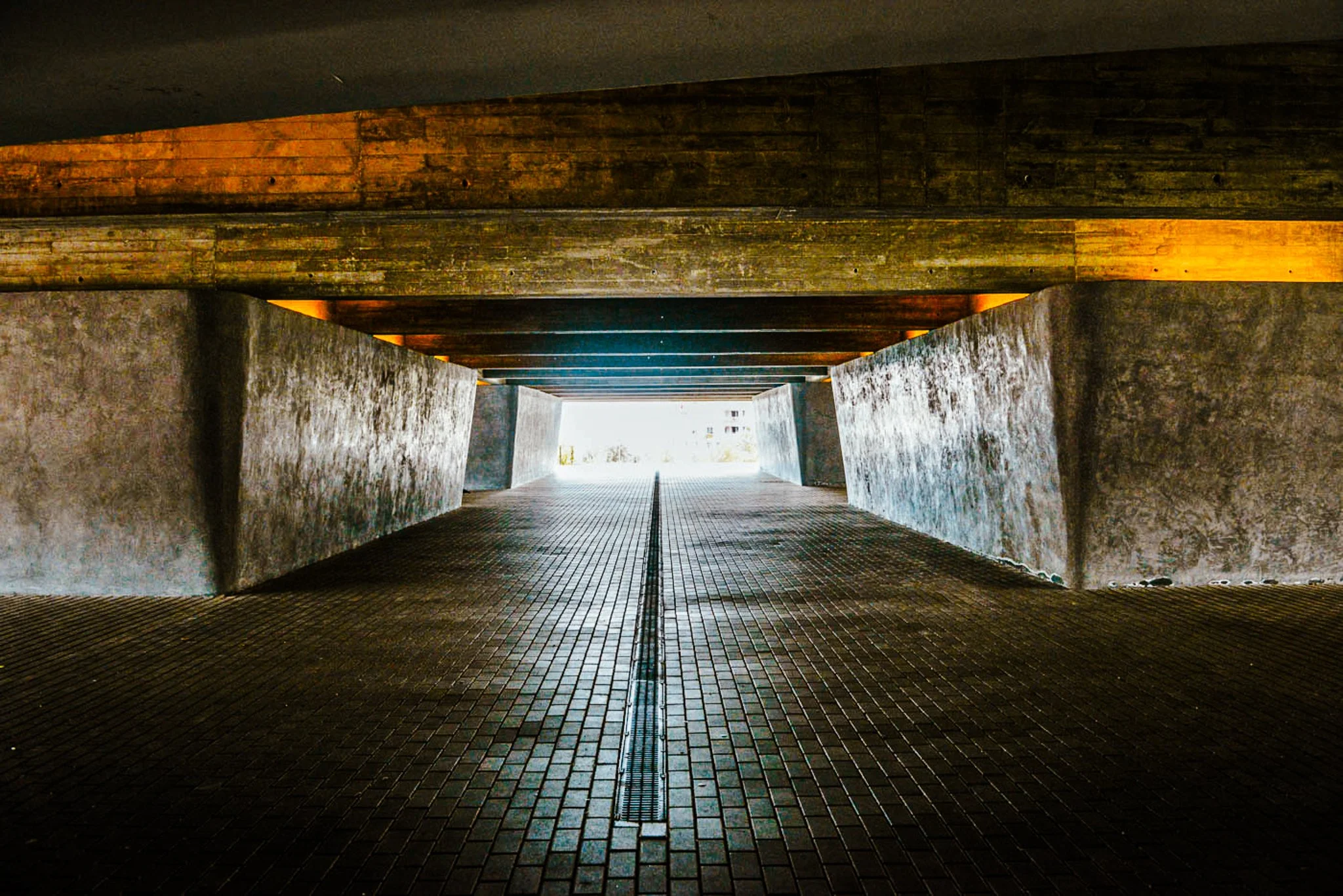 A film and photo location in Portugal from walnut films, Underpass with brick pavement, concrete walls, and wood beams overhead, illuminated by warm orange lighting.