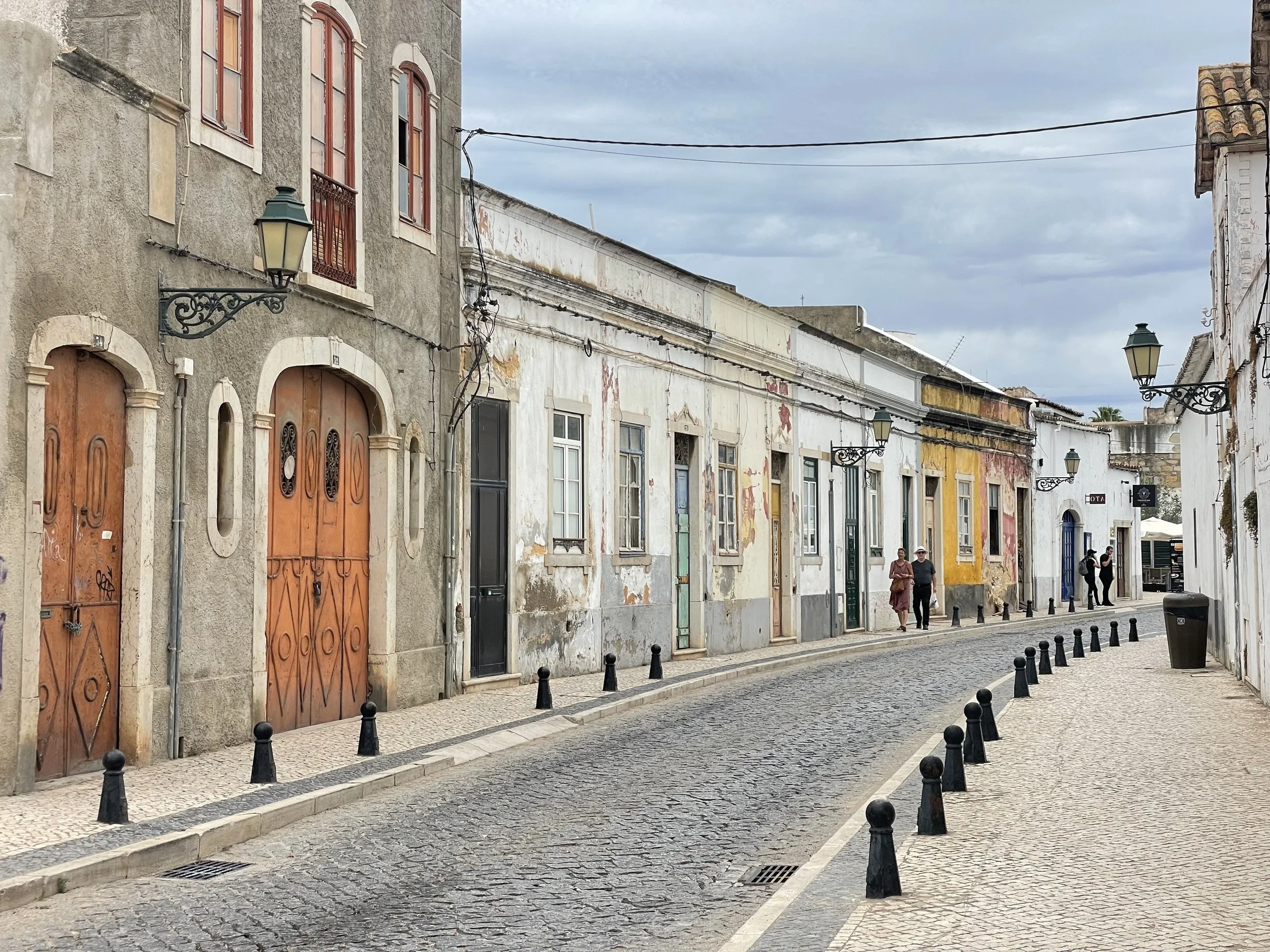 A film and photo location in Portugal from walnut films, Street view of old buildings with colorful, weathered facades, cobblestone road, street lamps, and a few pedestrians.”}
