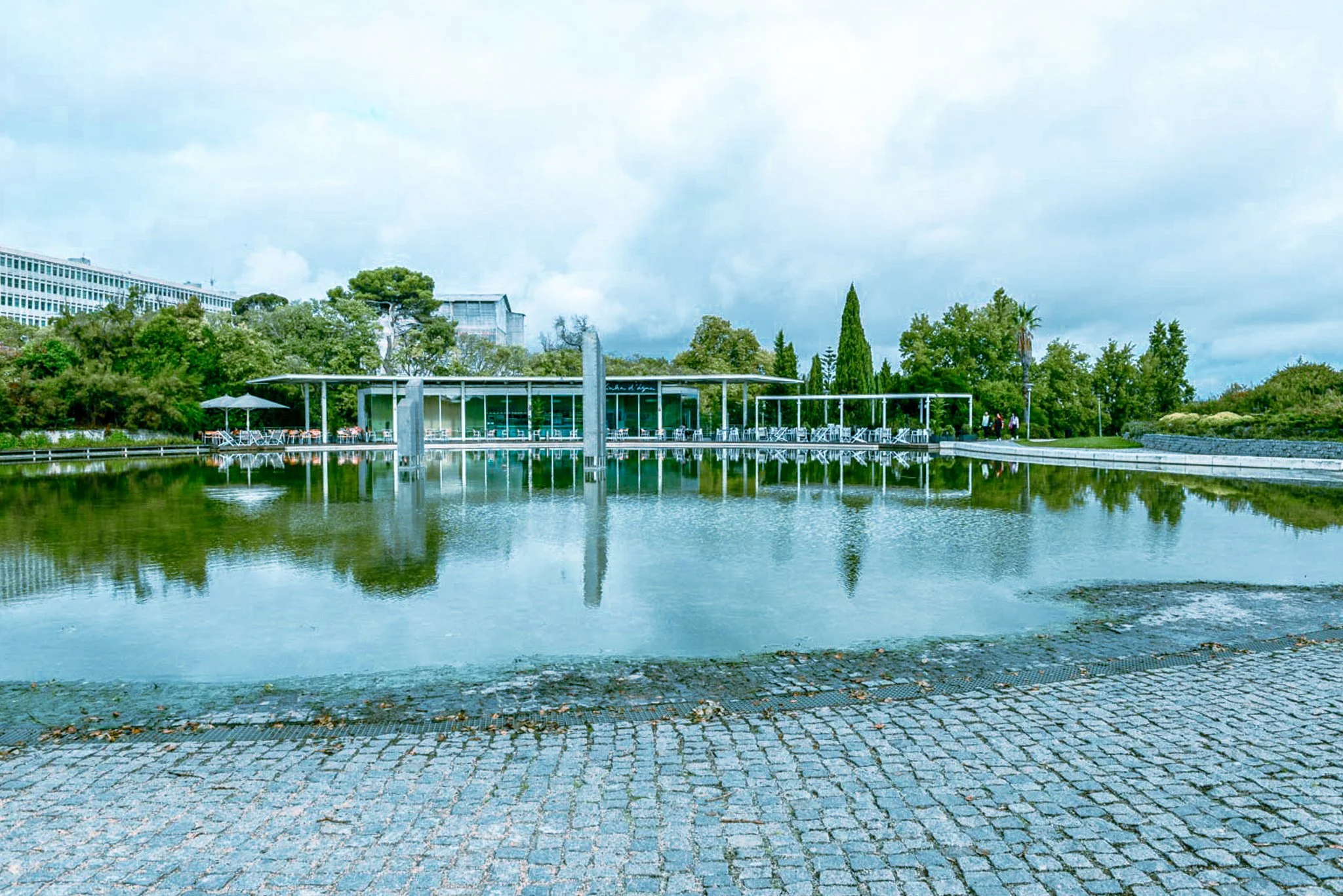 A film and photo location in Portugal from walnut films, A modern building with large glass windows, surrounded by trees, and a reflecting pool in the foreground. There is a paved circle in front of the pool and some outdoor seating, 