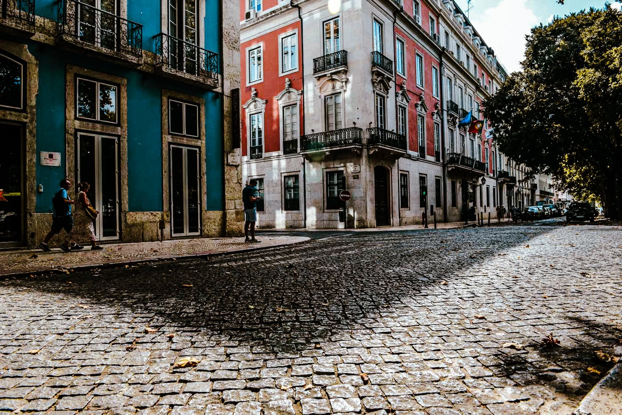 A film and photo location in Portugal from walnut films, Street view of colorful European-style buildings with ornate window frames and balconies, cobblestone street, and people walking.