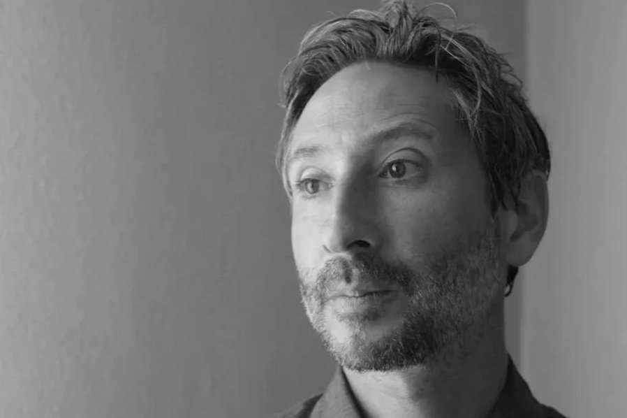 Black and white portrait of a middle-aged man with light, slightly wavy hair and a beard, looking contemplatively to the right.