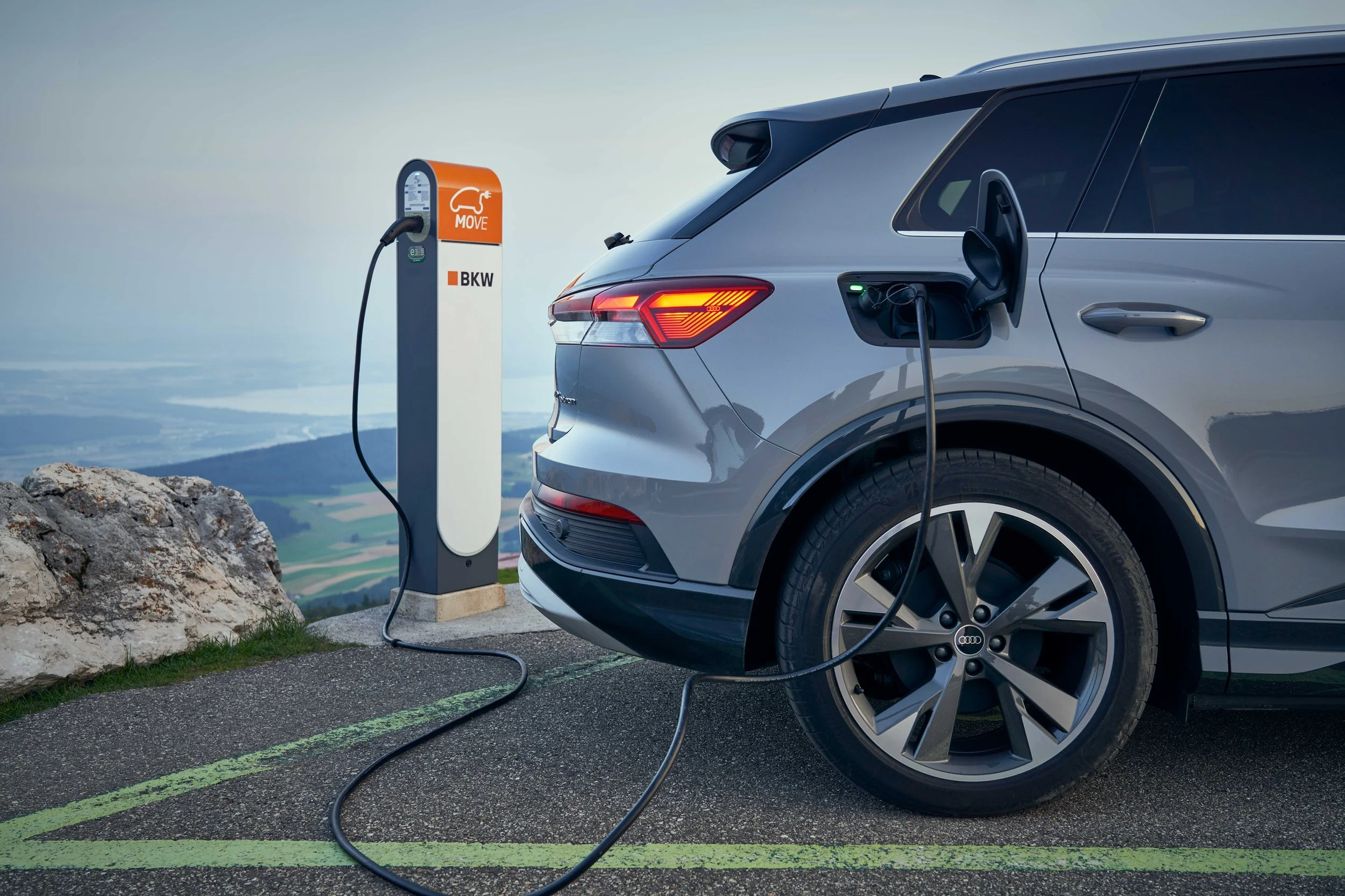 An electric silver-colored SUV parked in a mountain parking lot, connected to a charging station for charging.