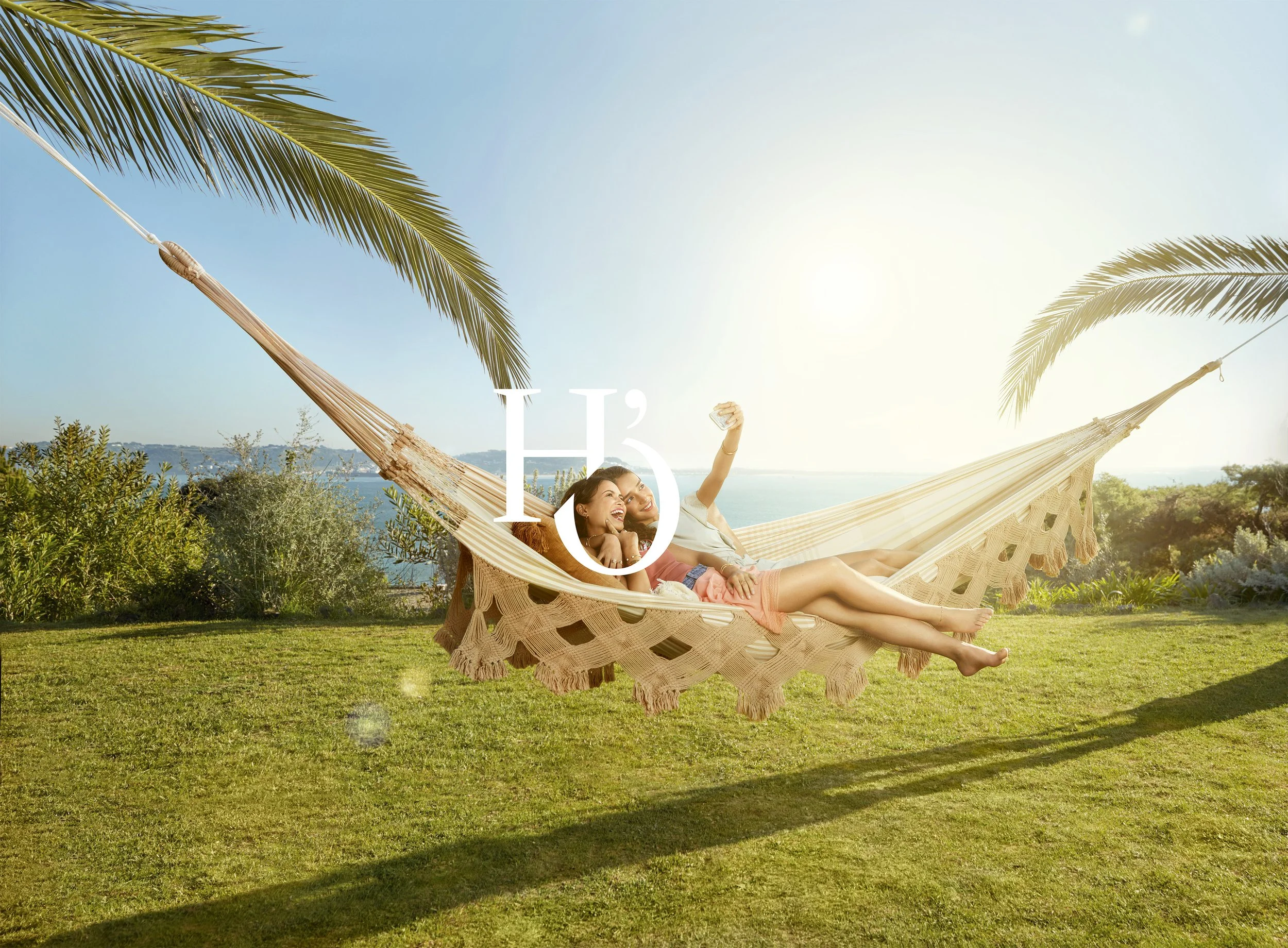 Two people lying in a hammock outdoors with palm trees and a blue sky.