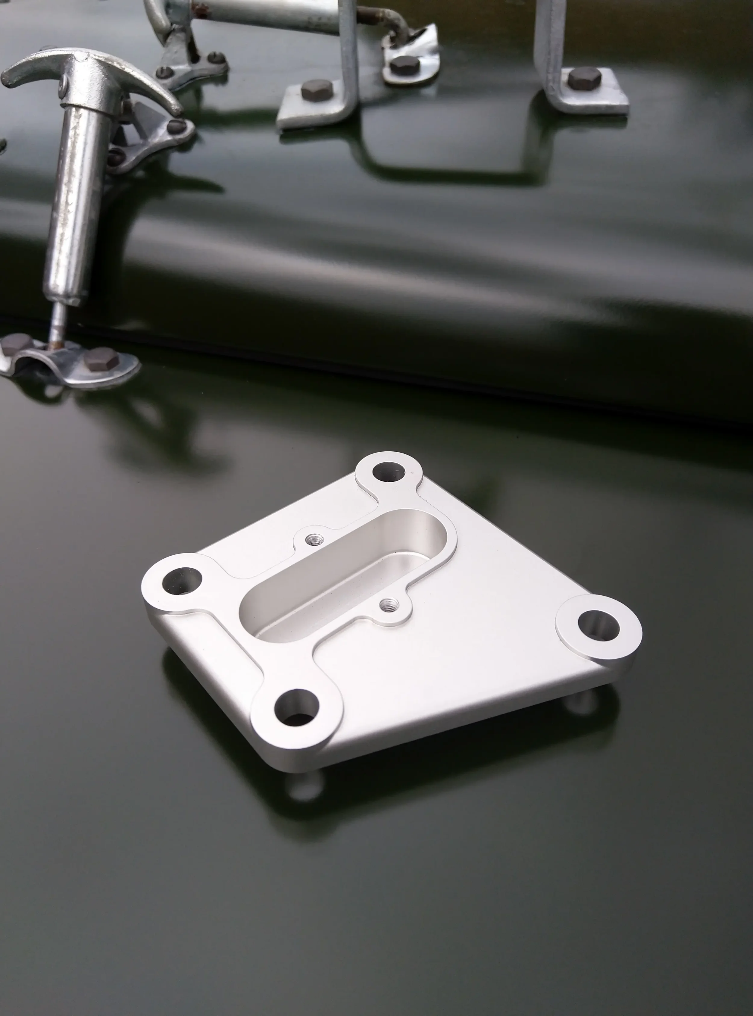 Close-up of metal mechanical parts, including a silver-colored machined component with multiple holes and a white mounting bracket, on a black surface.