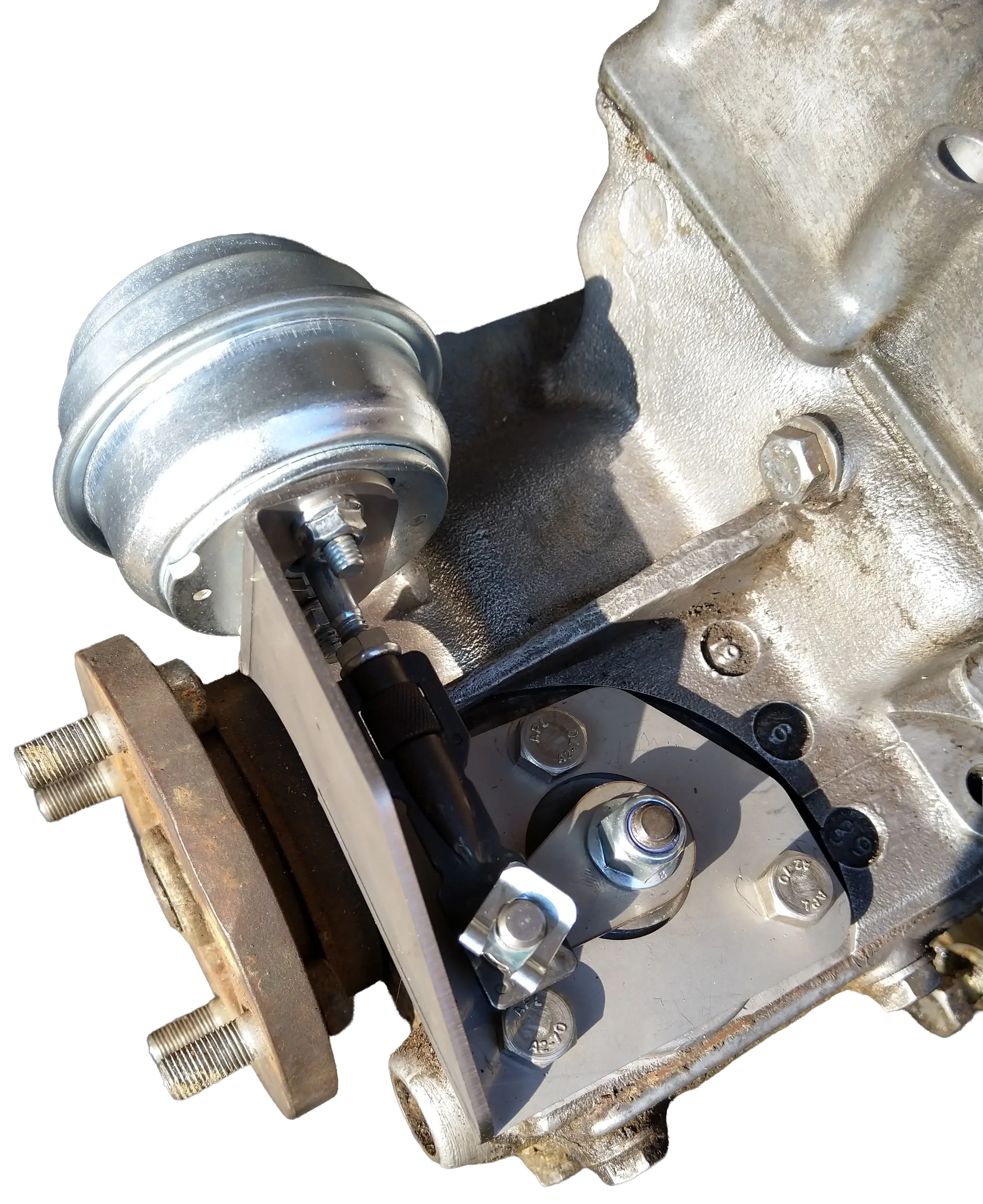 Close-up of a metallic engine component with bolts, screws, and a round pulley or gear attached to the metal surface.