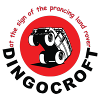 Logo featuring a stylized dump truck inside a red circle with black and white detailing, and text surrounding it that reads 'at the sign of the prancing land rover DINGOCROFT'.
