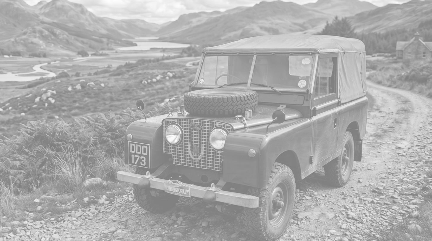 A vintage Land Rover vehicle on a rural dirt road with a scenic landscape of hills, water, and a house in the background.