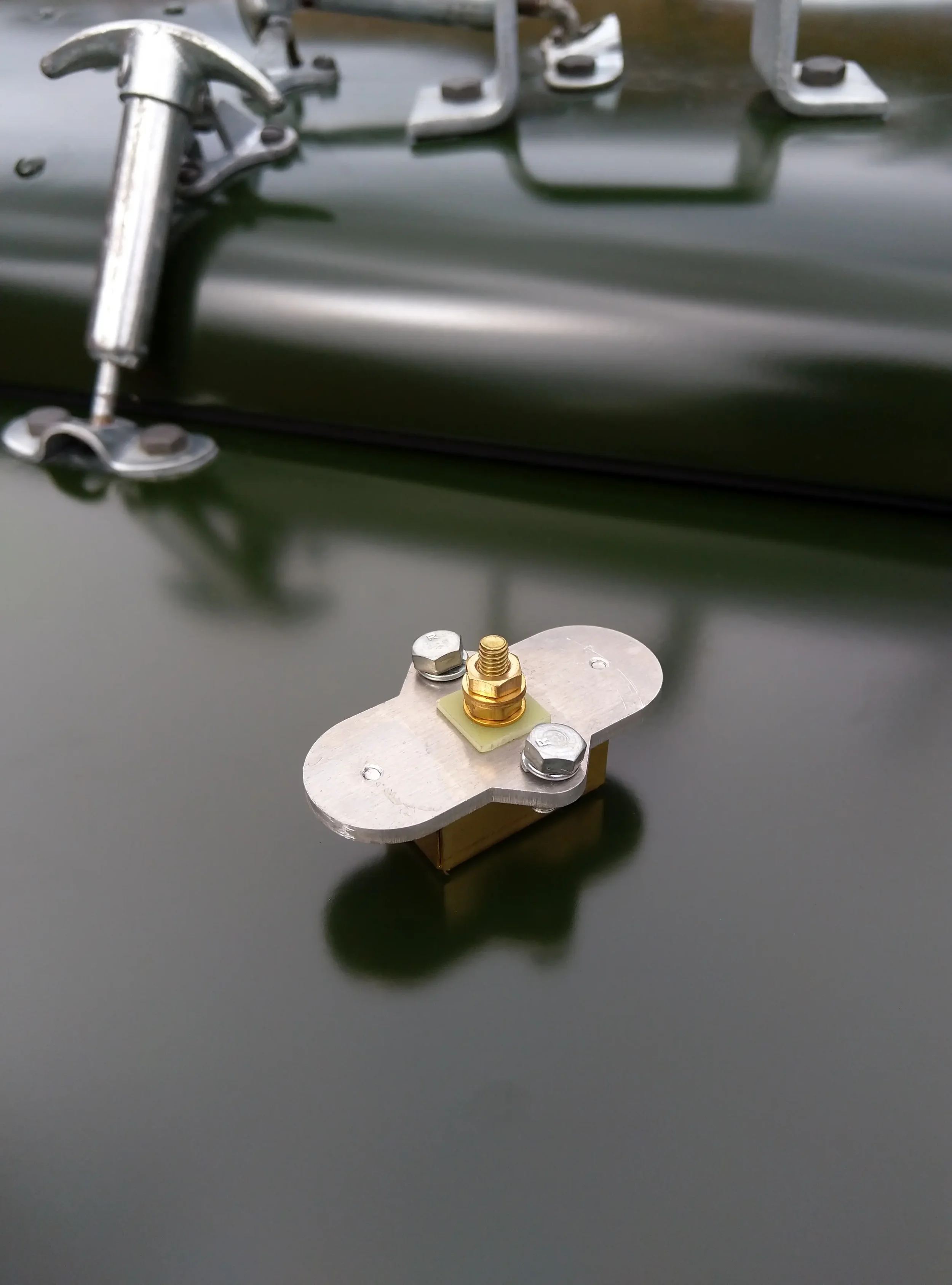 Close-up of metallic hardware and a brass antenna post mounted on a black surface, possibly a panel or vehicle.