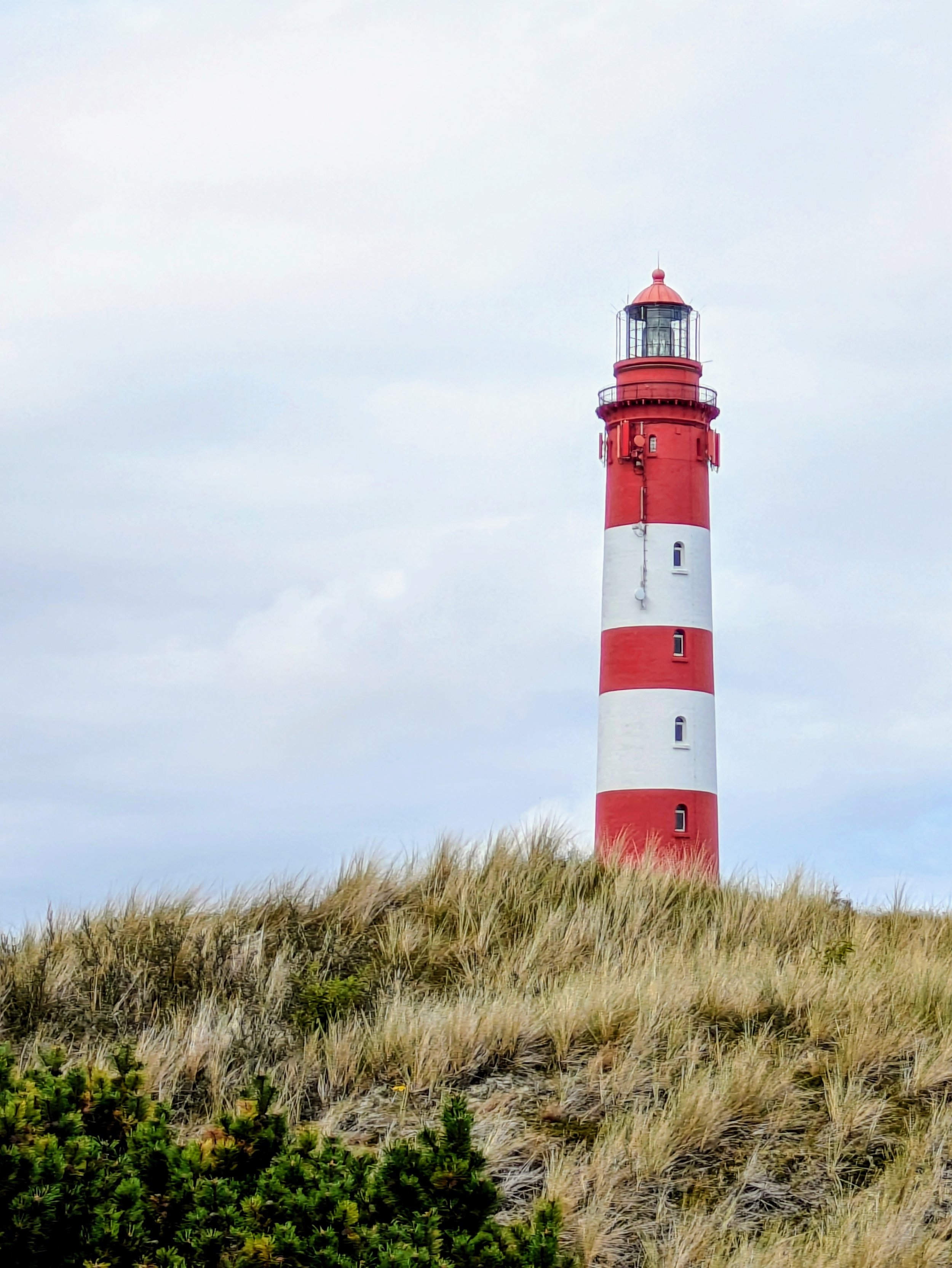 Leuchtturm auf einer Sanddüne mit Gräsern. Der Himmel ist bewölkt.