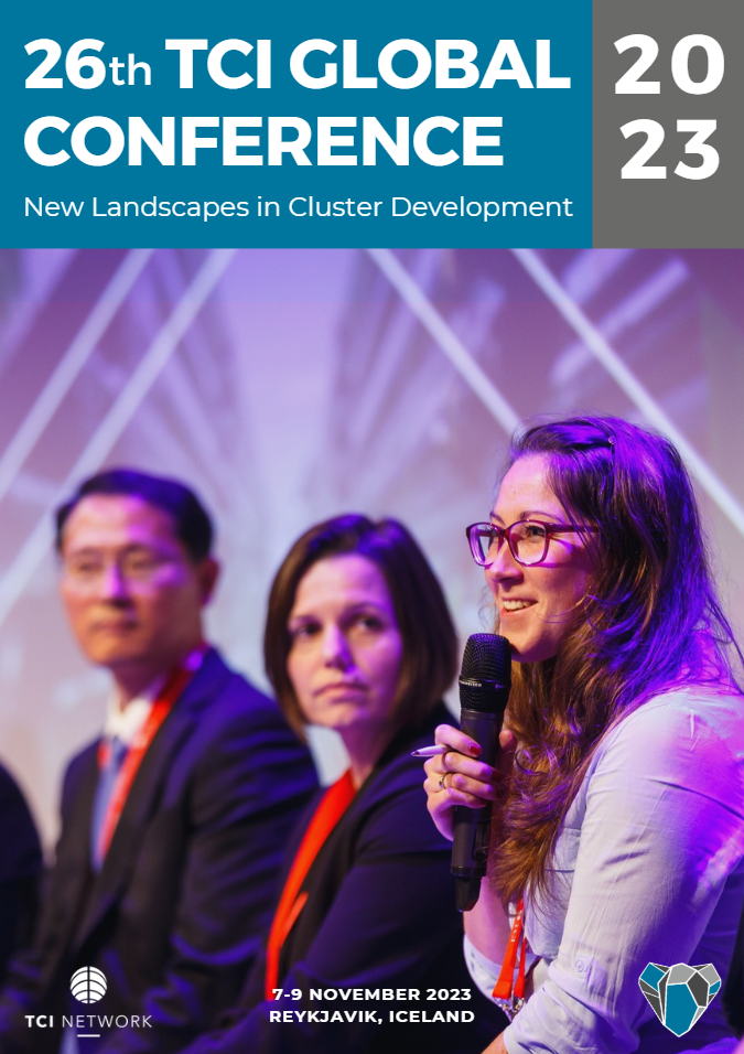 Panel of three people at the 26th TCI Global Conference held in Reykjavik, Iceland, November 7-9, 2023. The woman on the right is speaking into a microphone, with two others, a woman and a man, sitting beside her. The background features stage lighti