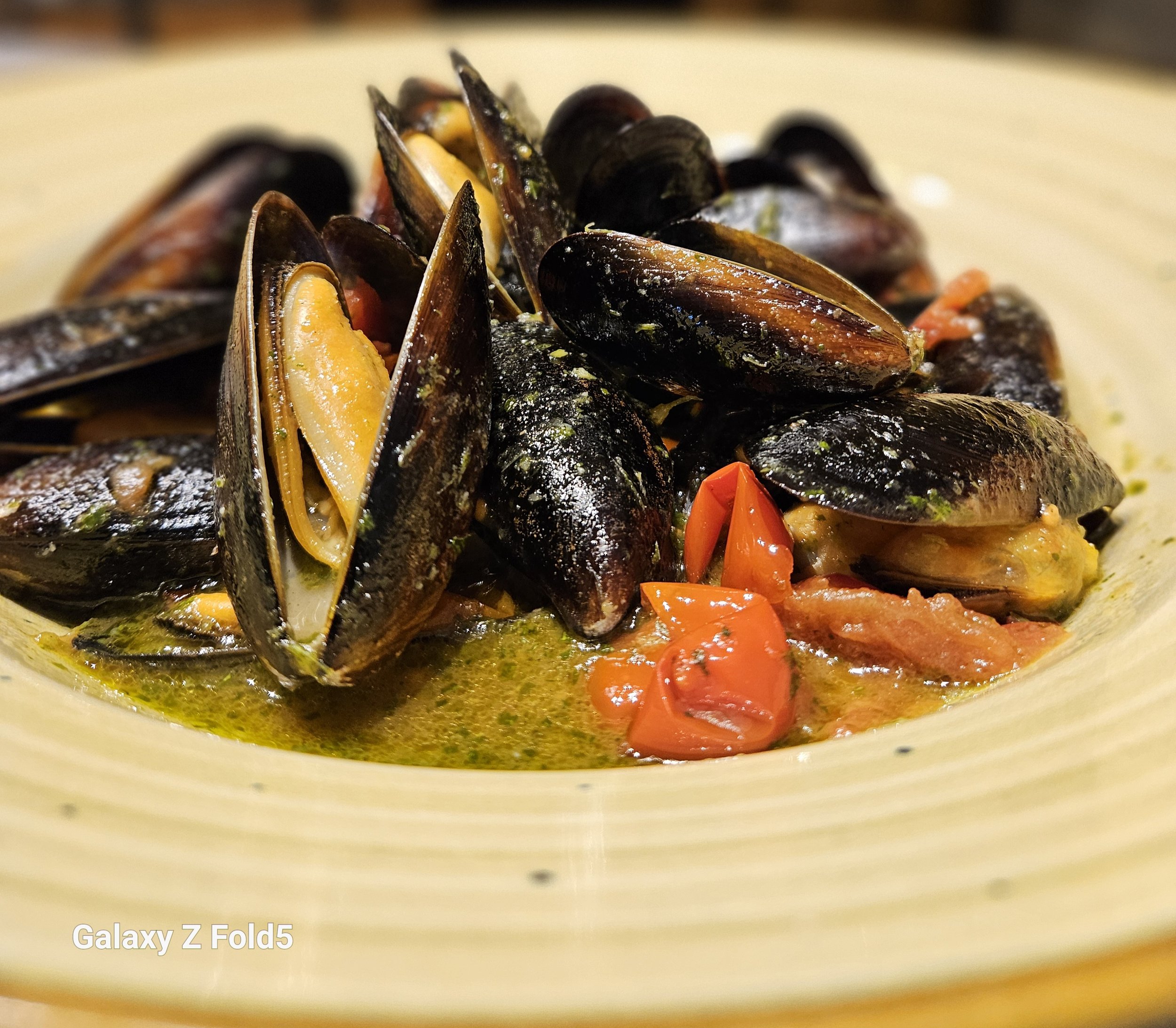 Close-up of a bowl of mussels cooked in a sauce with red peppers and herbs