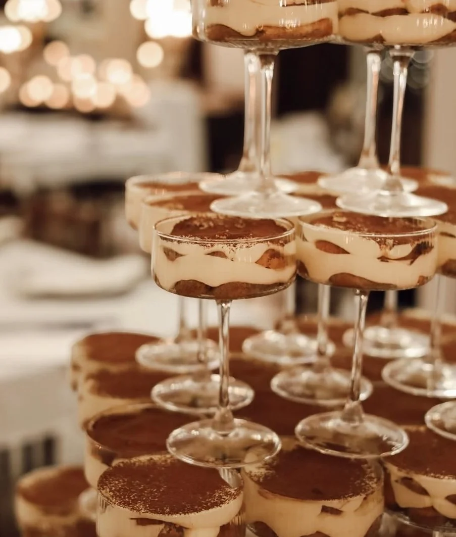 A tiered display of individual tiramisu desserts in glass cups with dusted cocoa powder on top.