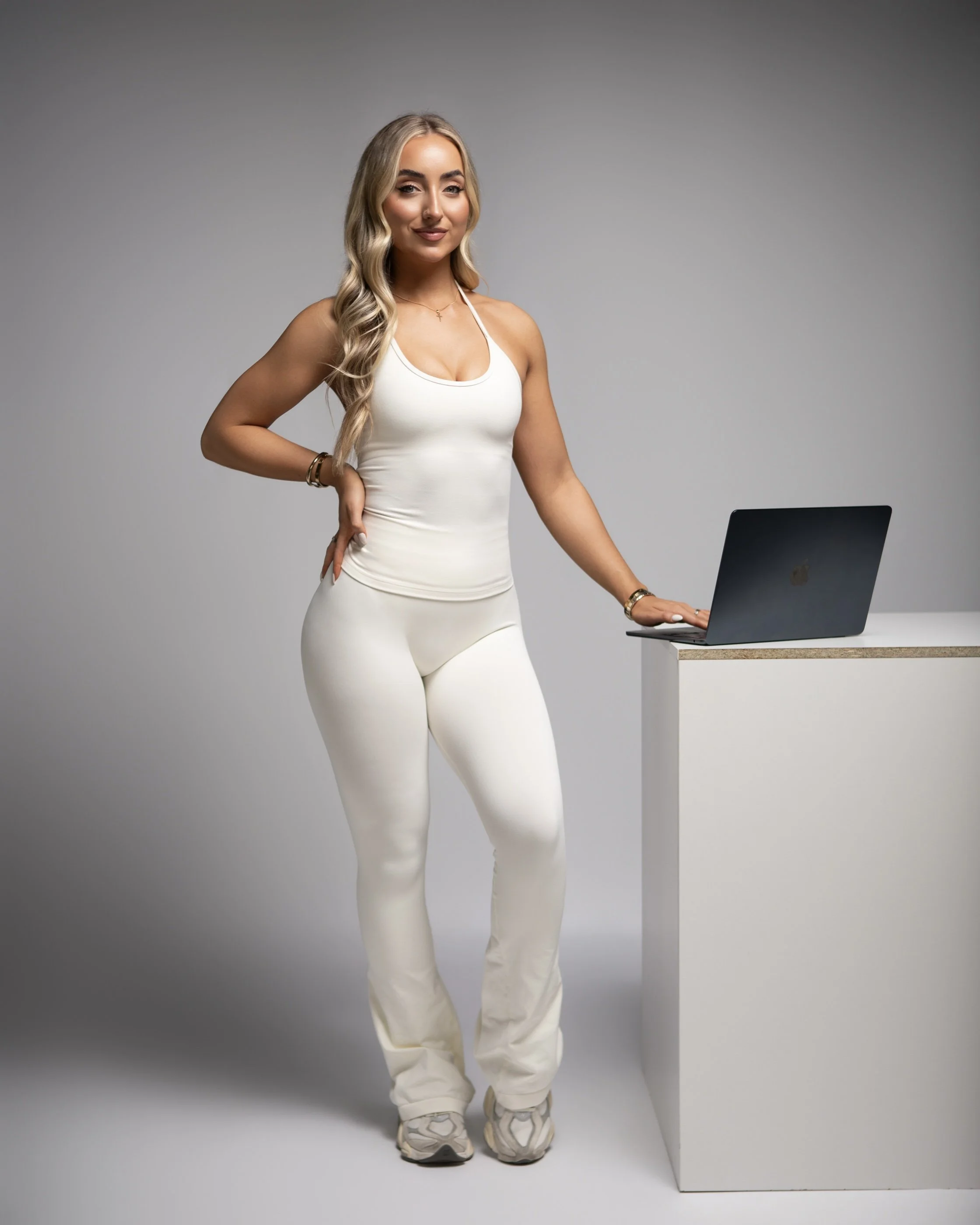 Olivia Strauss, founder of Olura Coaching, women's online fitness coach standing beside a laptop in a white activewear set.